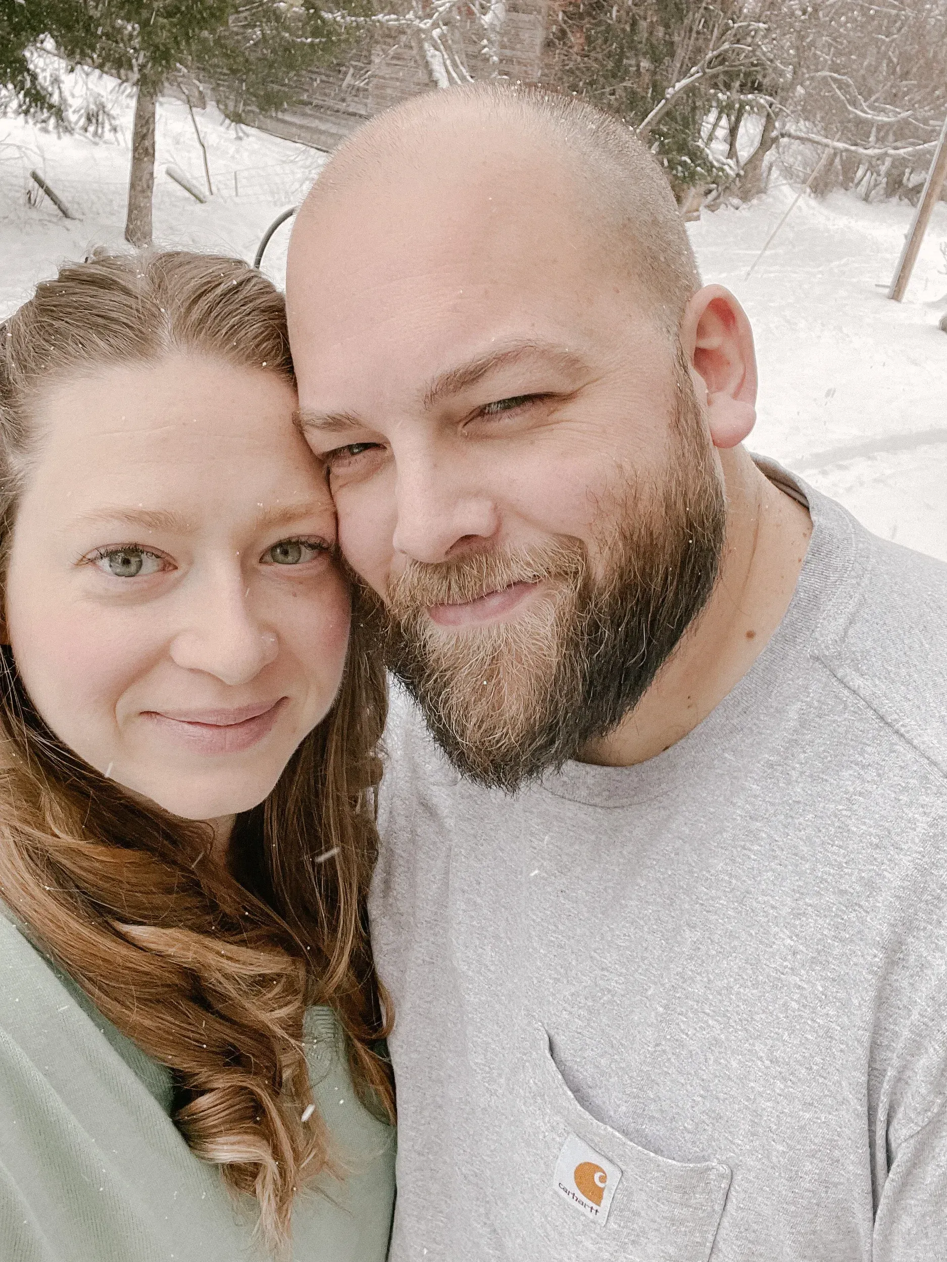Two people smiling outdoors in the snow, bundled in winter clothing.