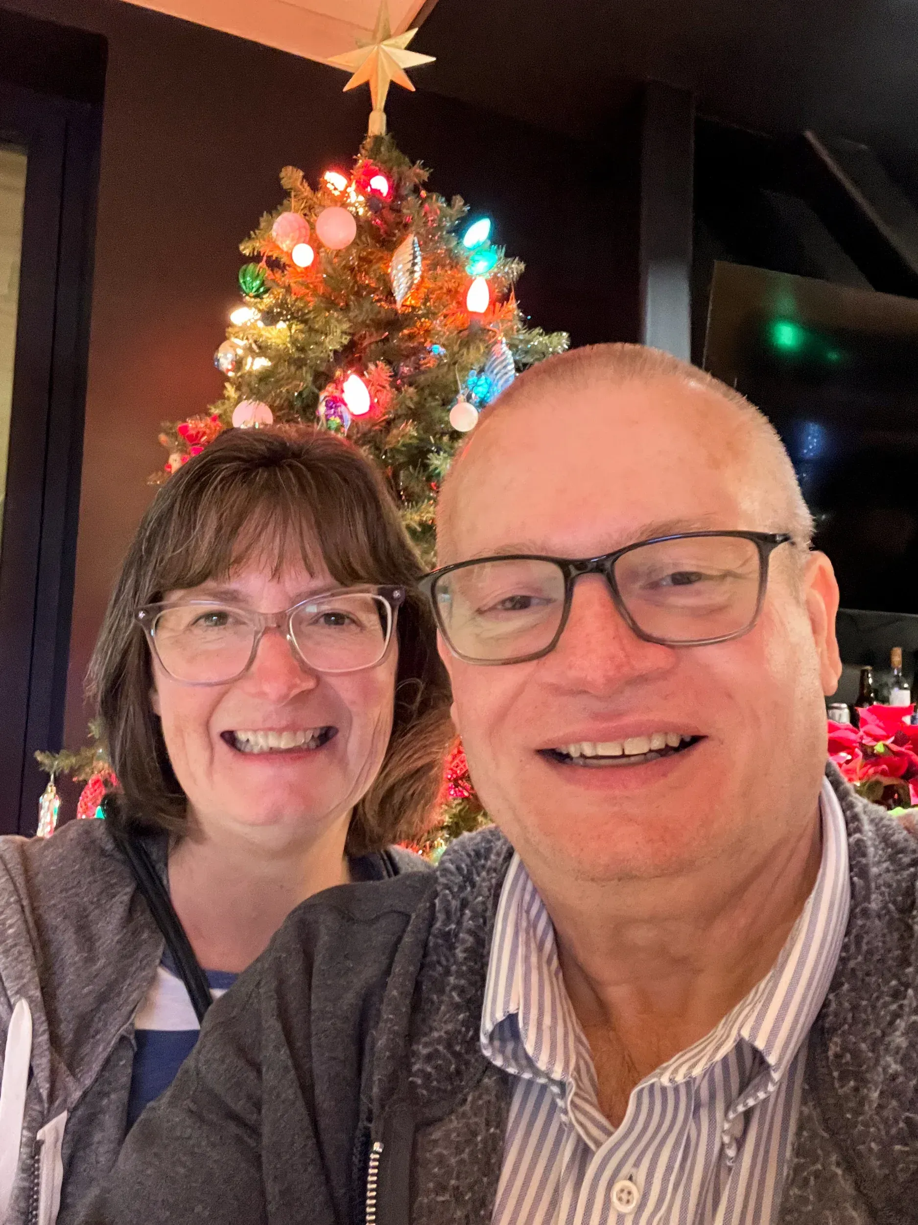 Smiling couple posing indoors beside a lit Christmas tree