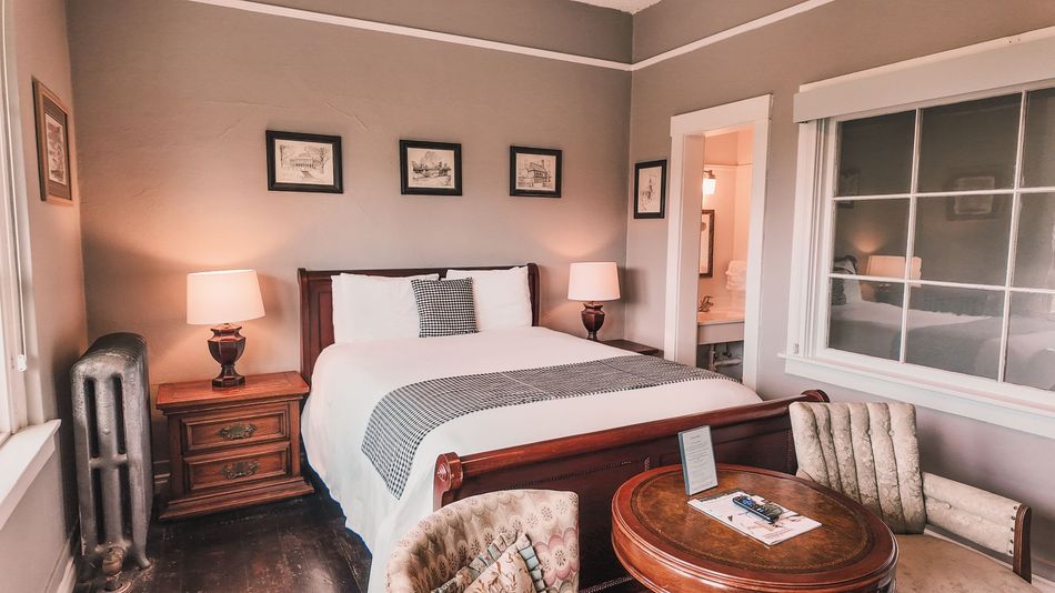 Cozy bedroom with a white bed, bedside lamps, framed art, and a small seating area by a window.