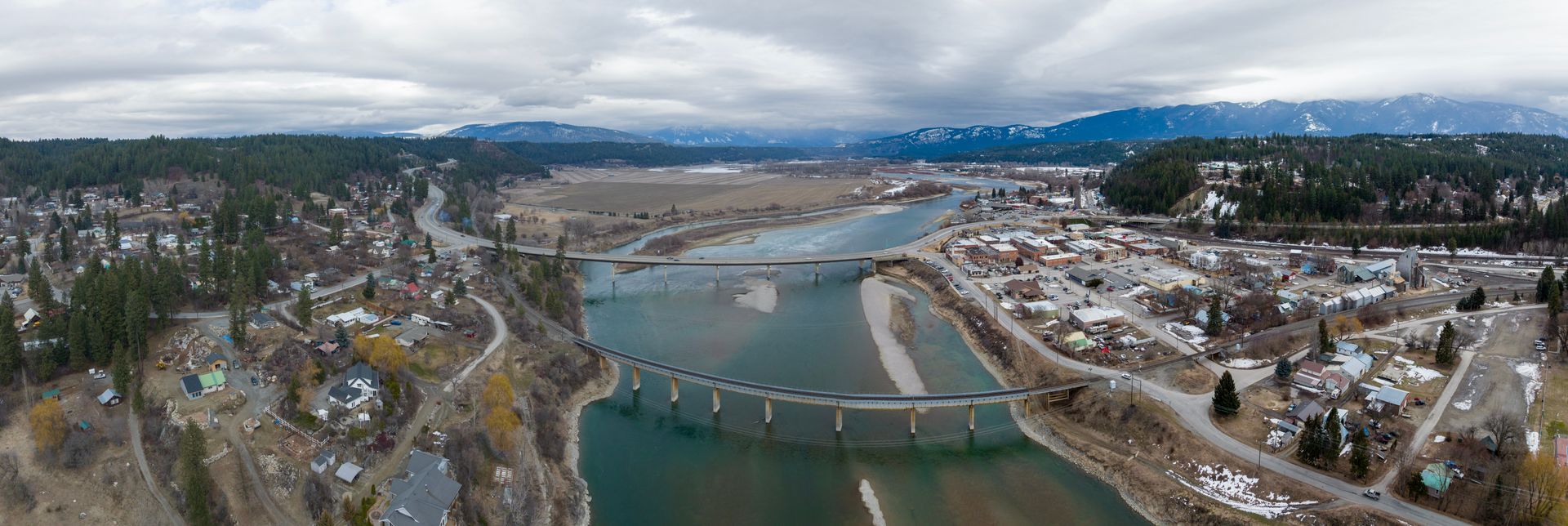 Aerial view of a river separating two town sections, connected by a road bridge and a multi-arched railway bridge.