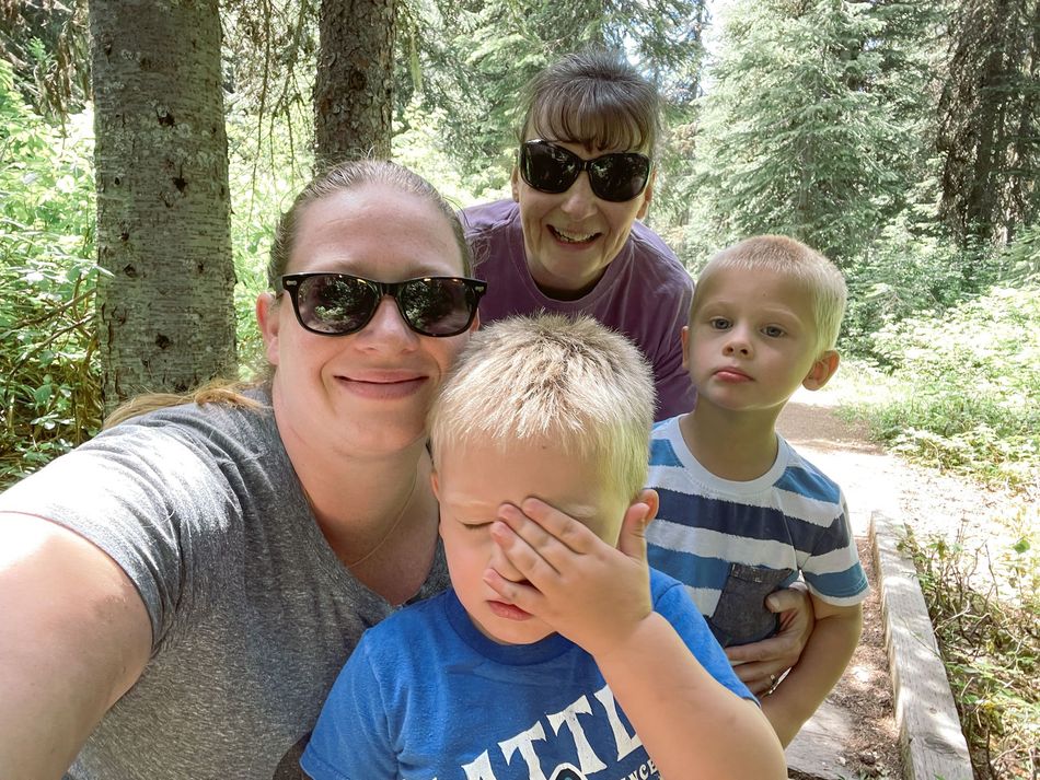 Three people and a child taking a selfie on a forest trail, with one child covering their face.