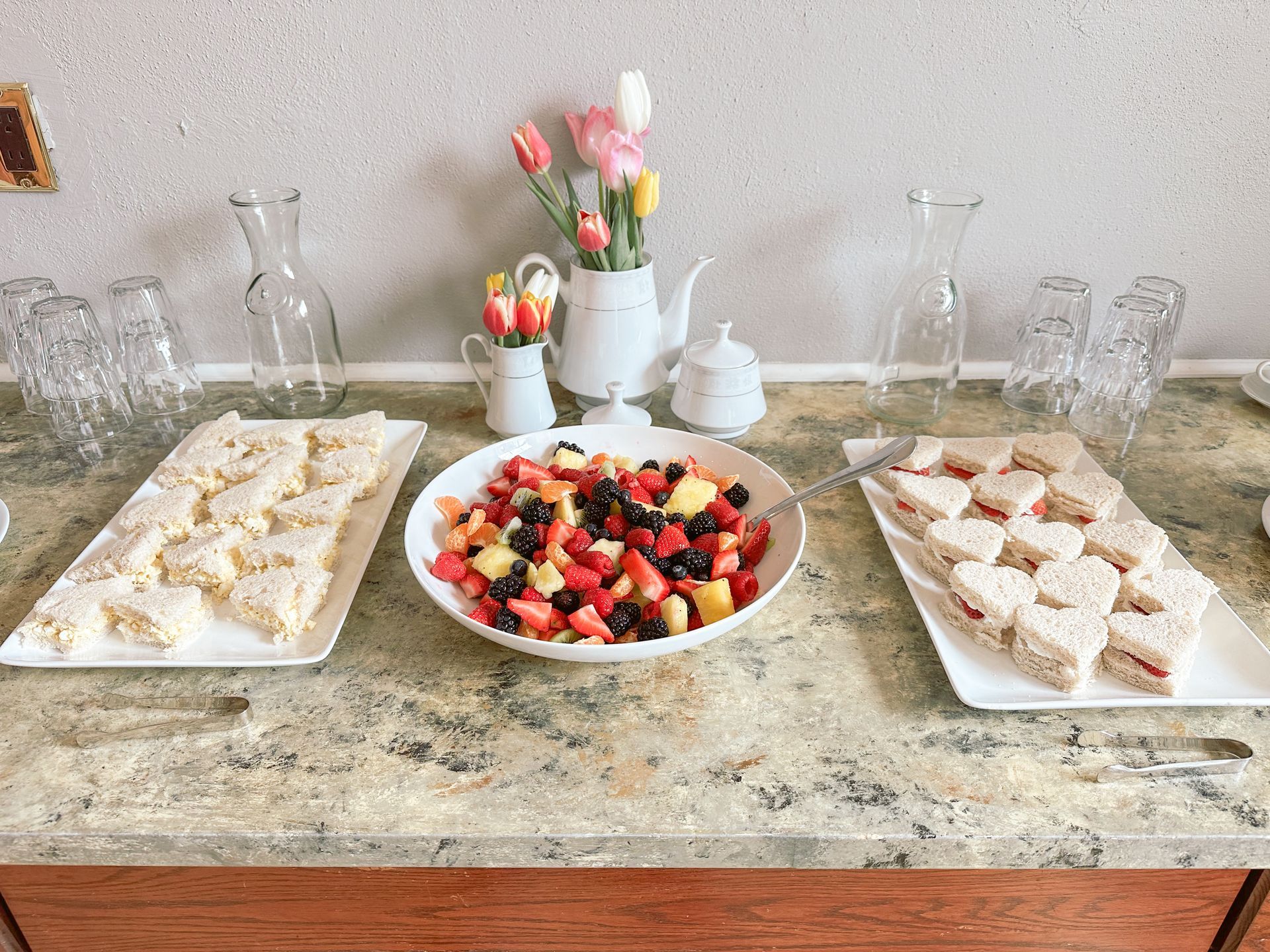 Dessert buffet with fruit salad and platters of pastries on a marble table with glassware and tulips