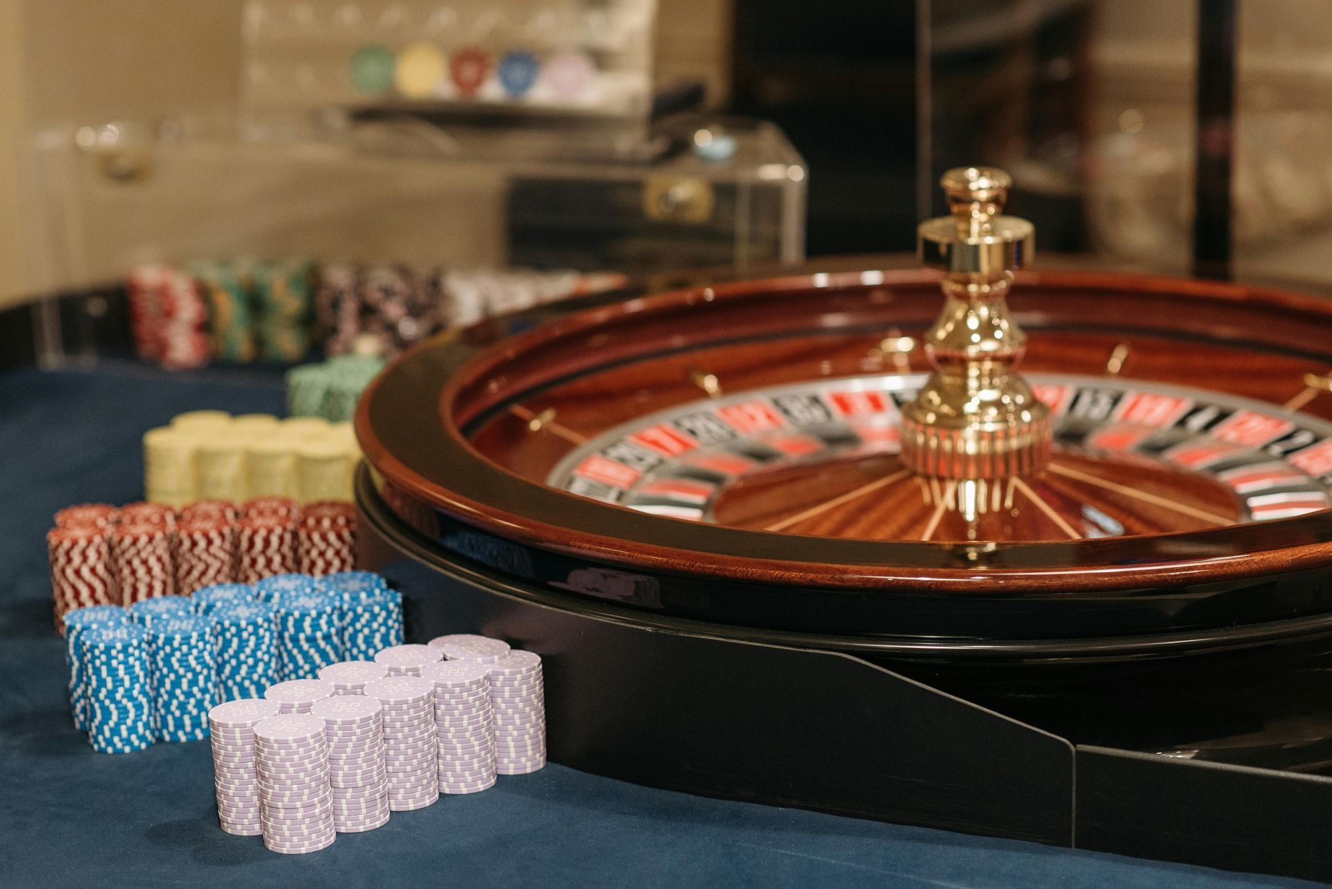 A roulette wheel sits on a blue surface surrounded by stacks of colorful casino poker chips.