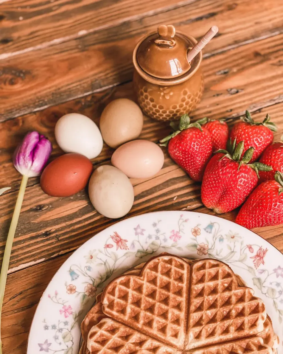 Waffle on floral plate with eggs, strawberries, and a teapot on a rustic wooden table