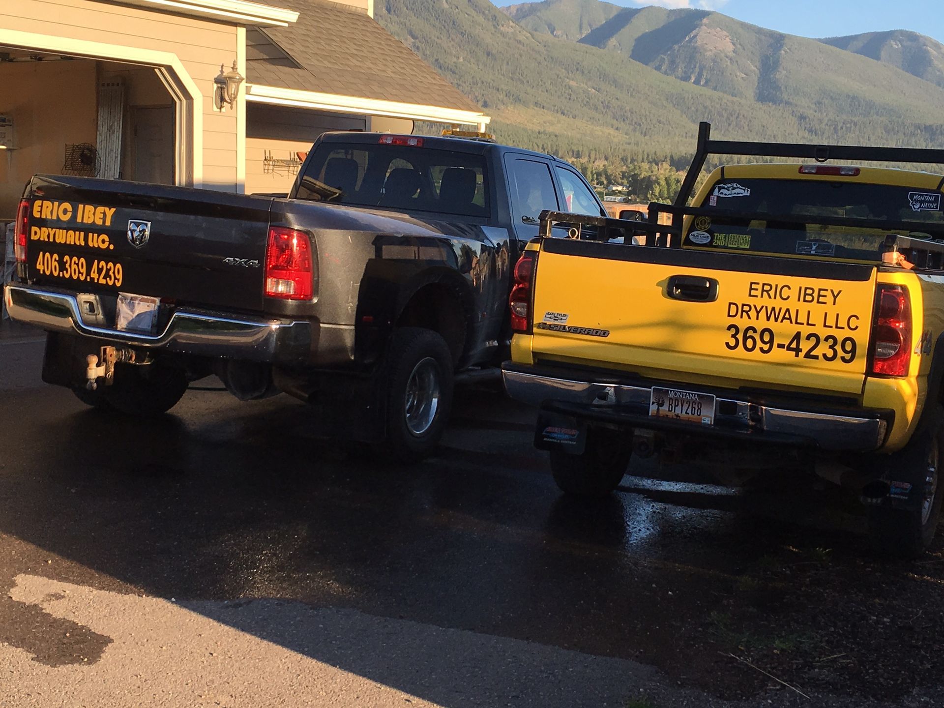 two trucks are parked in front of a house with mountains in the background