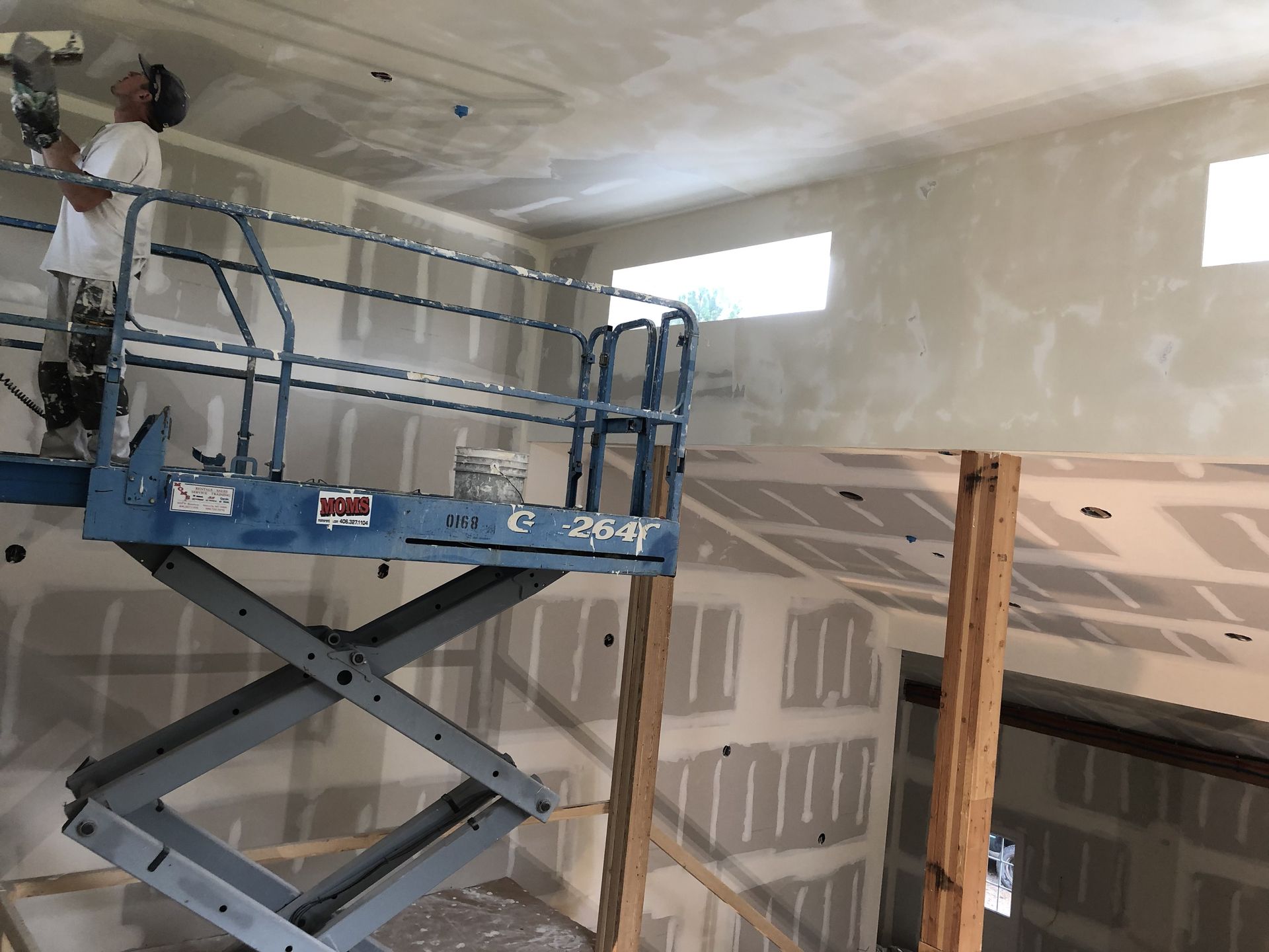 a man is standing on a scissor lift painting a wall .