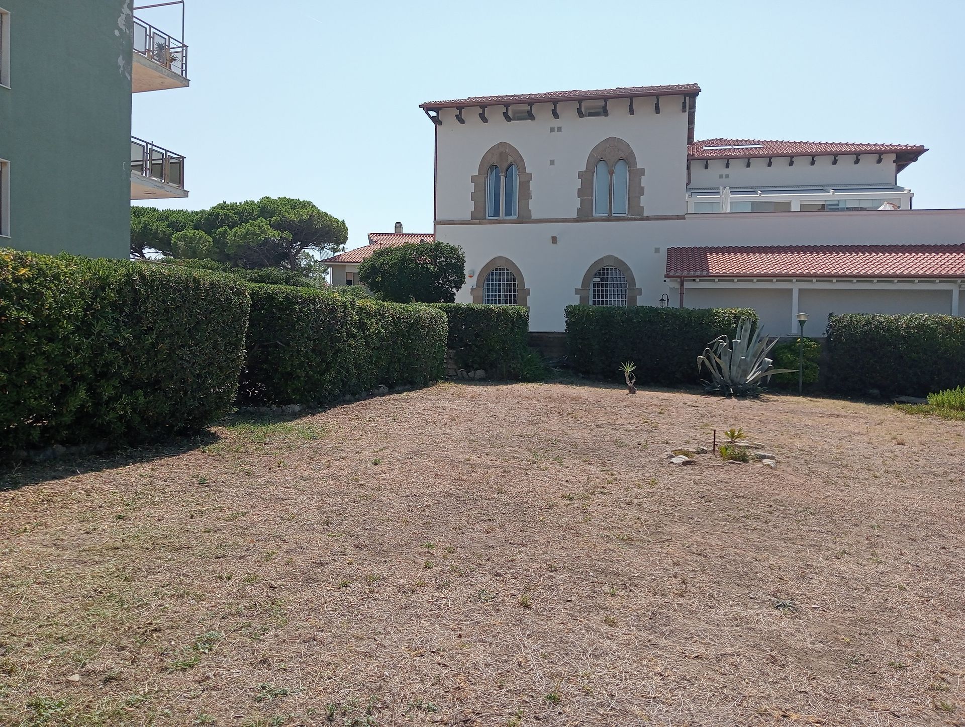 Un grande edificio bianco con un tetto di tegole rosse è circondato da cespugli e ghiaia