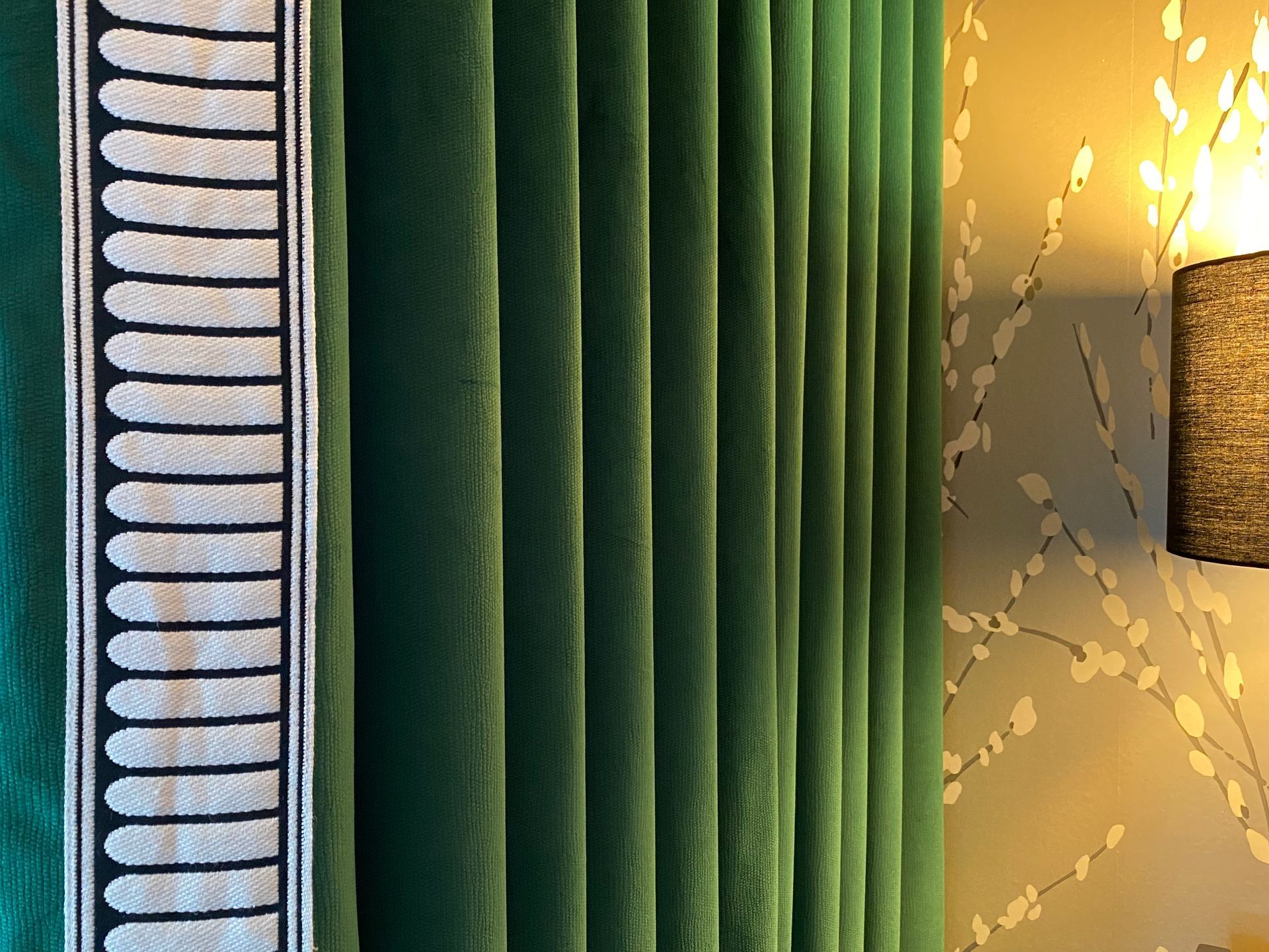 A close up of a green curtain in a room with a lamp.