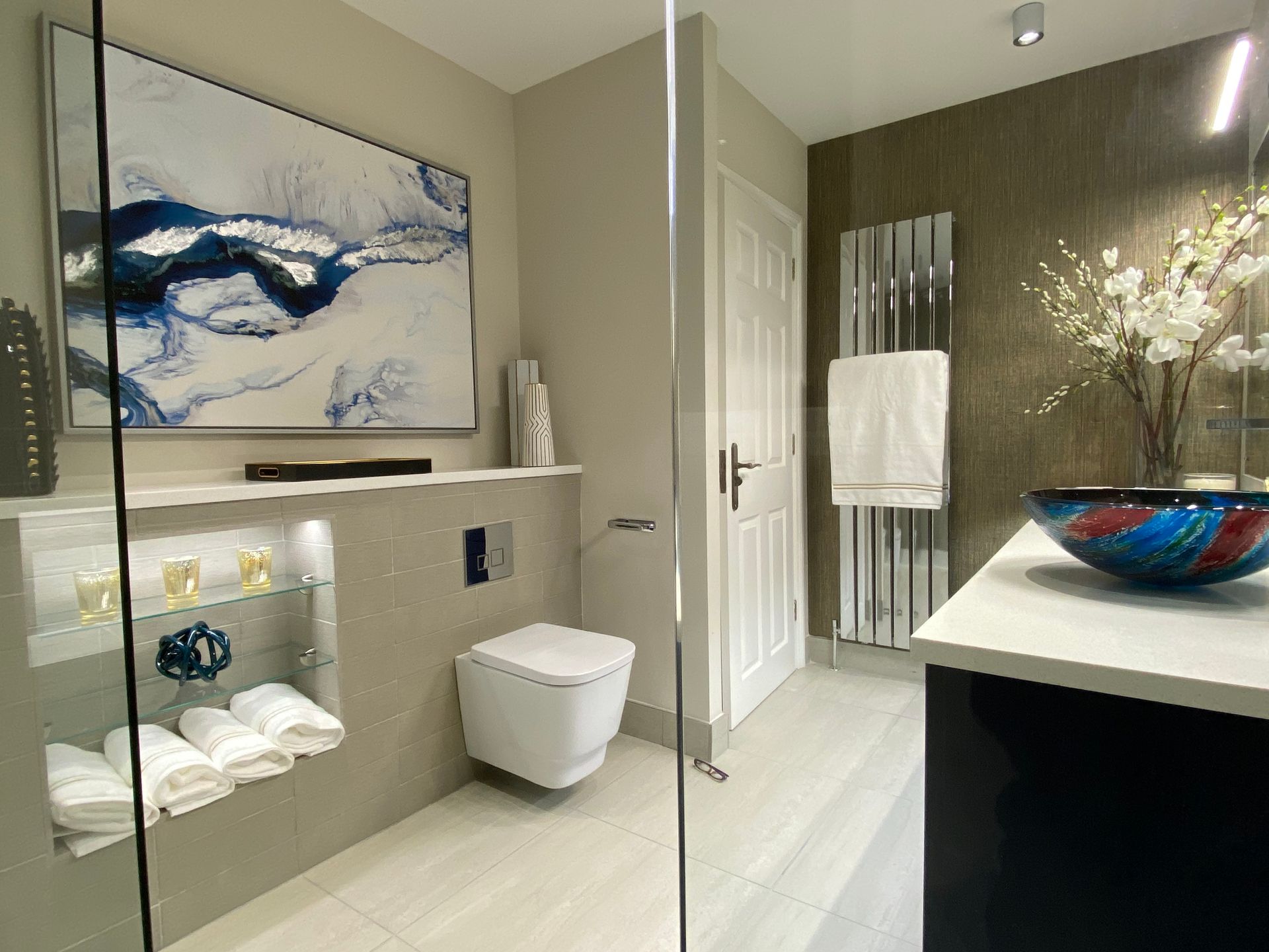 A bathroom with a toilet , sink and a painting on the wall.