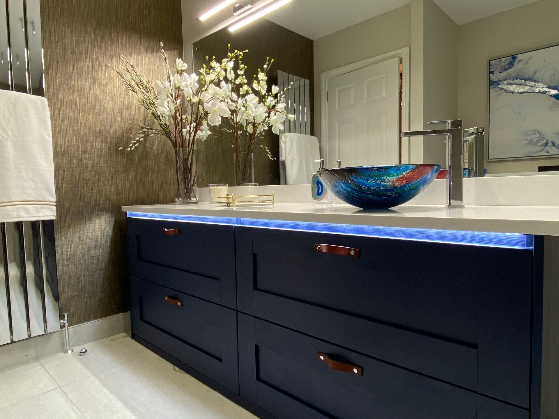 A bathroom with blue cabinets , a sink and a mirror.