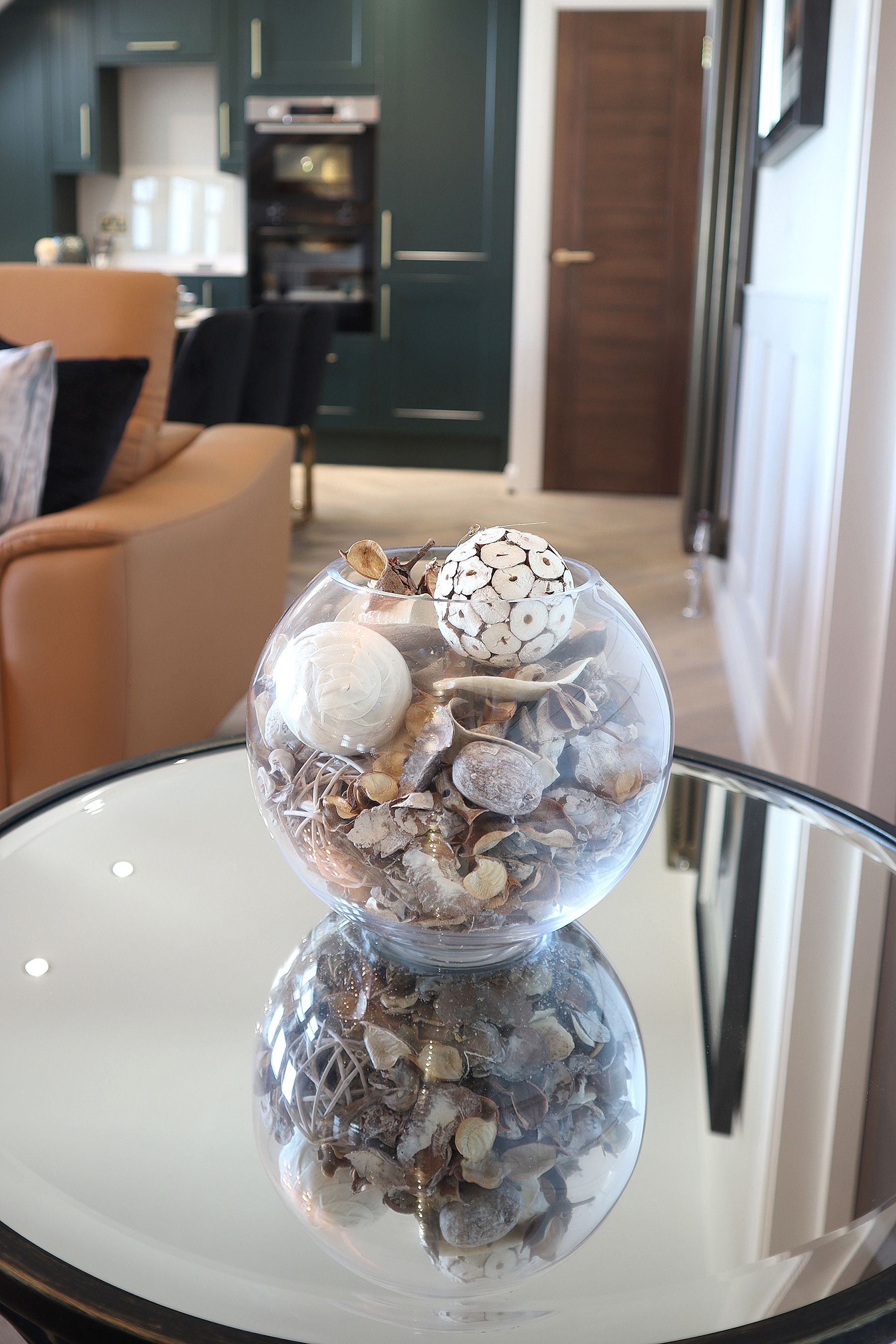 A glass ball filled with seashells is sitting on a glass table.