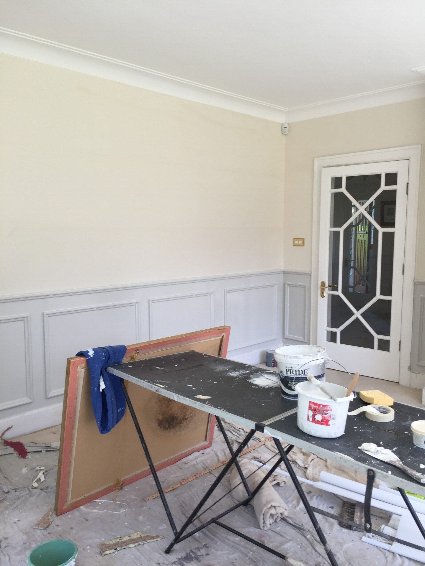 A table with a bucket of paint on it in a room with a door.