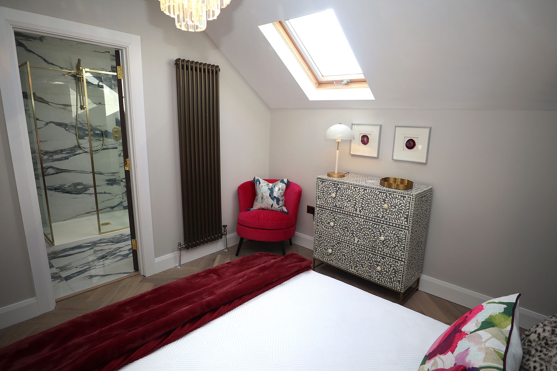 A bedroom with a bed , chair , dresser and skylight.