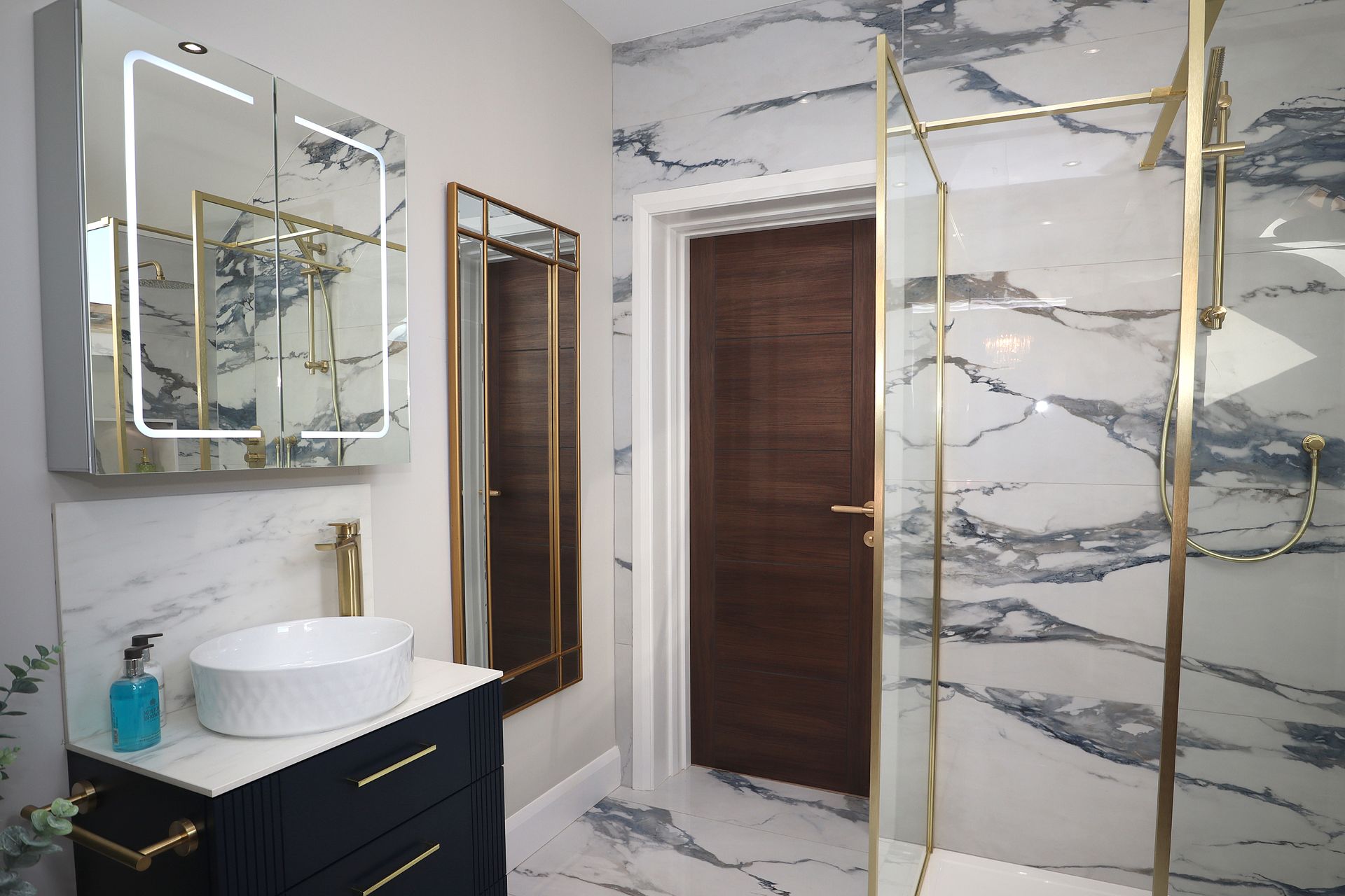 A bathroom with a sink , mirrors , and a walk in shower.