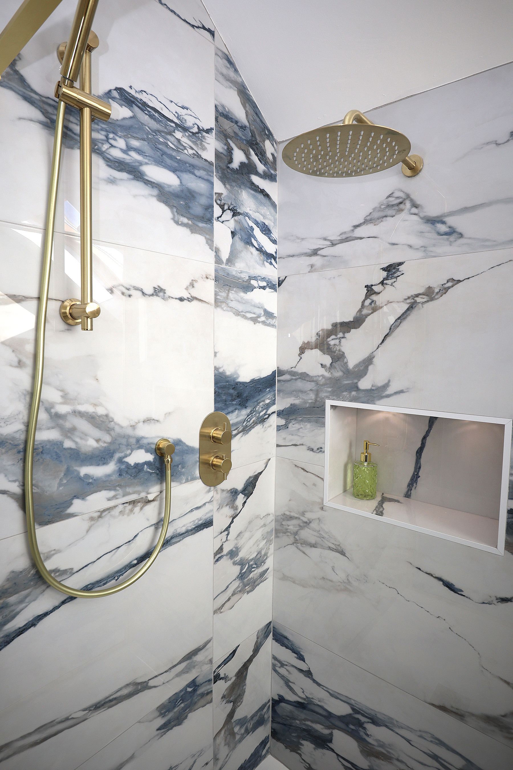 A shower with a marble wall and a gold shower head.