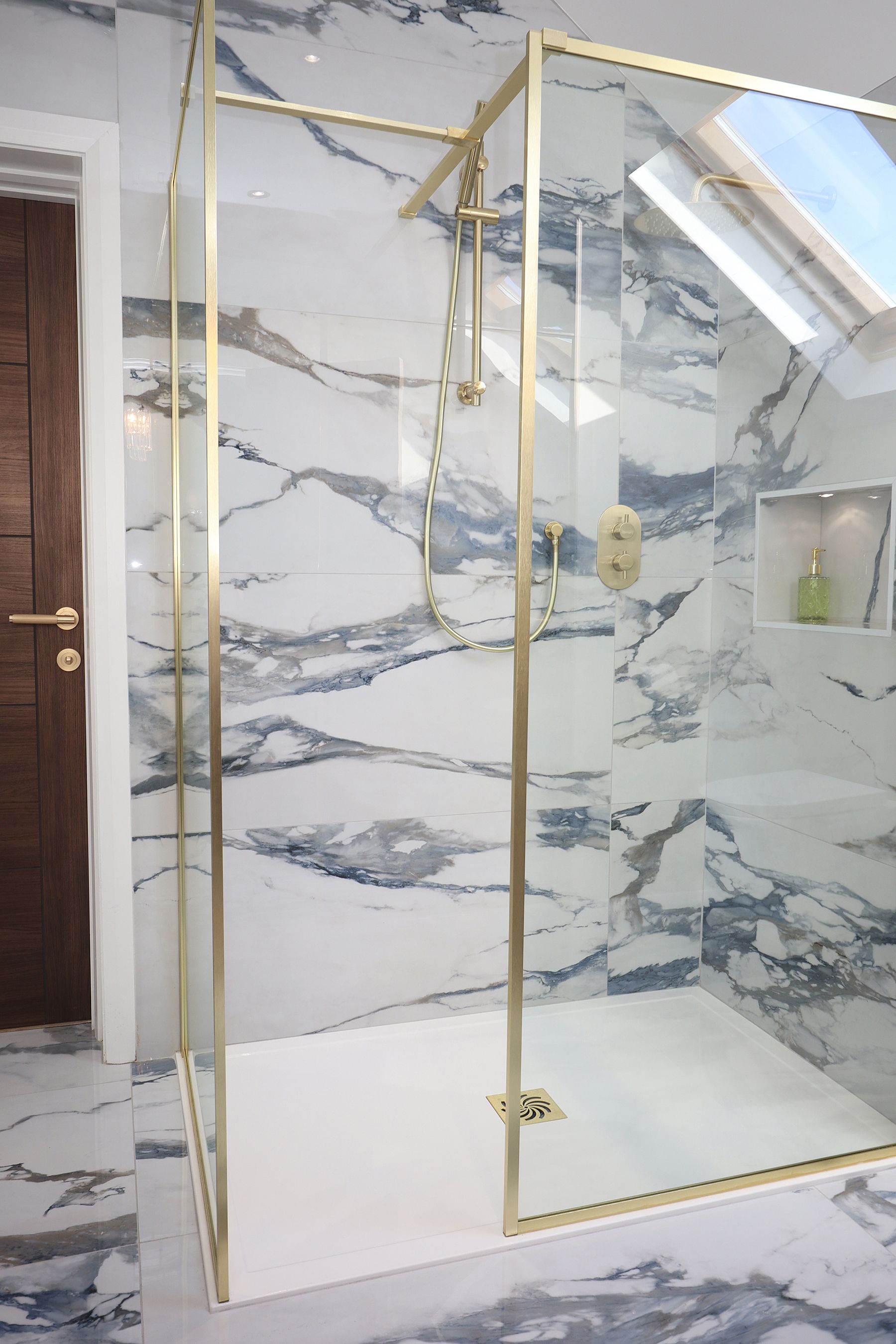 A bathroom with marble tiles and a walk in shower with a gold frame.