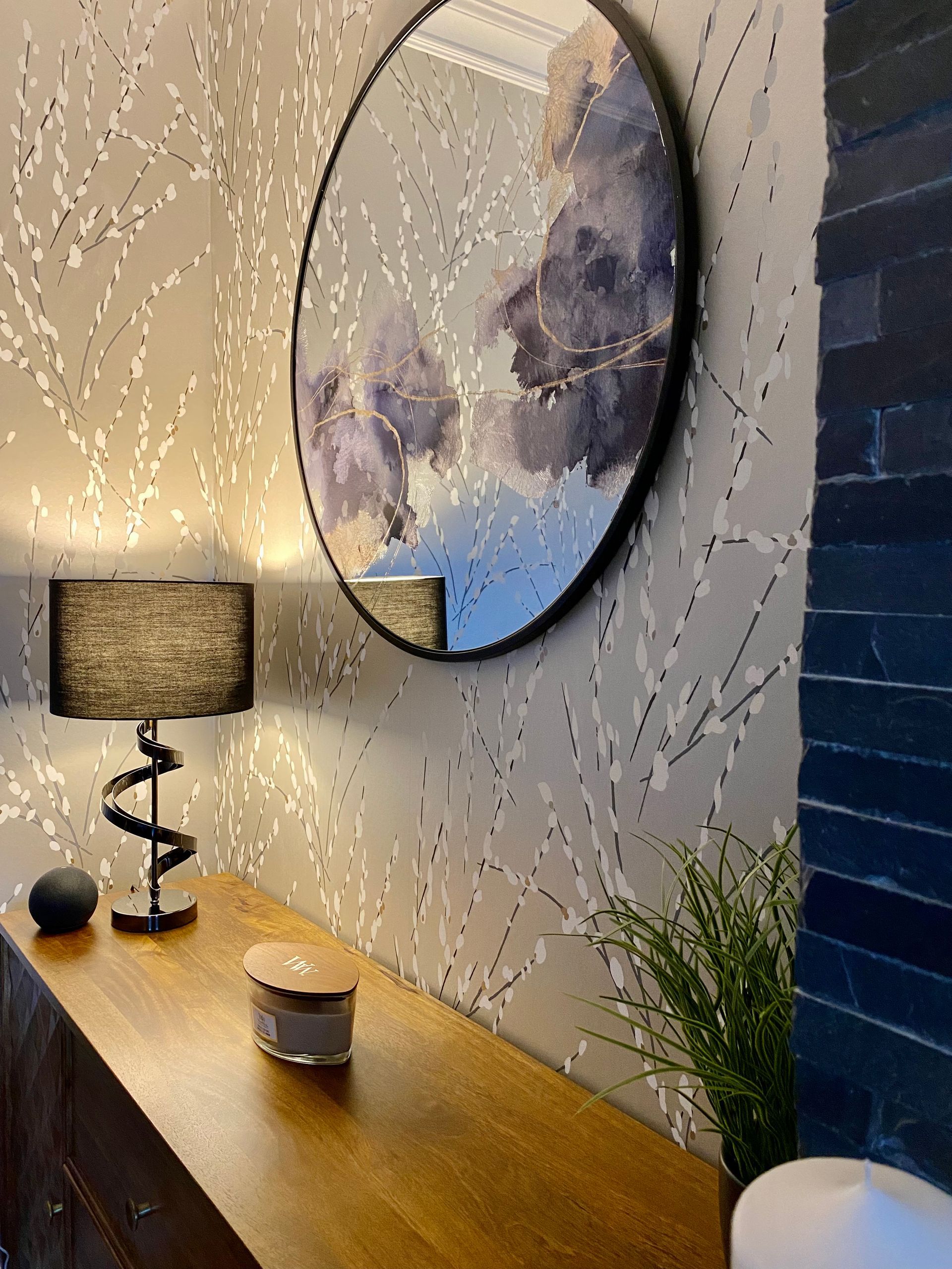 A round mirror is hanging on a wall above a wooden table.