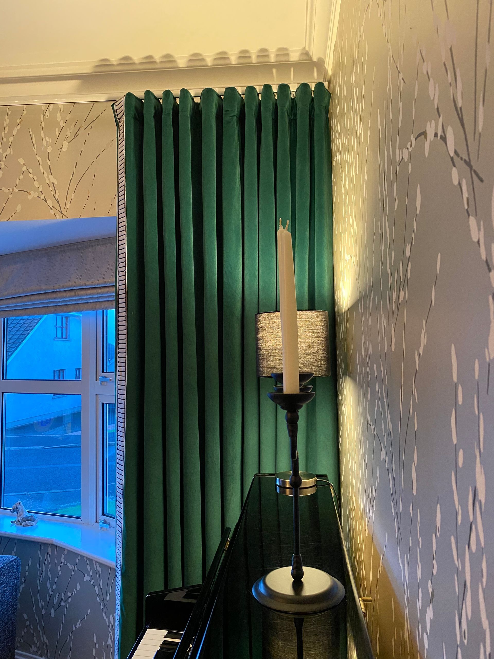 A living room with green curtains , a piano , a lamp and a candle.
