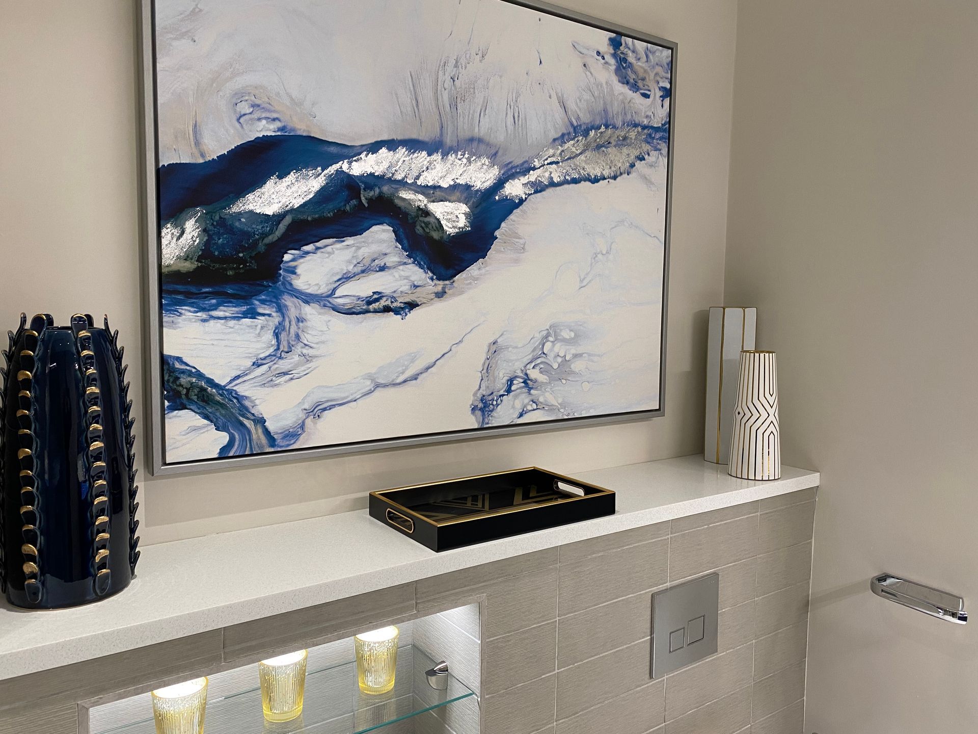 A bathroom with a painting on the wall and a vase on the shelf.