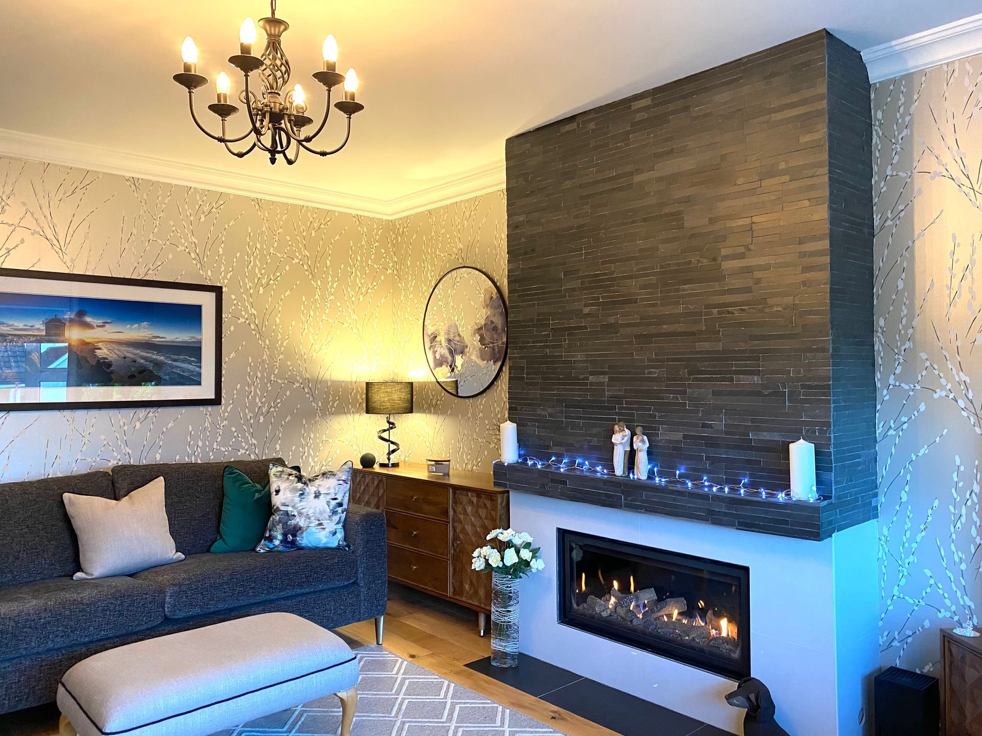 A living room with a fireplace , couch , ottoman and chandelier.