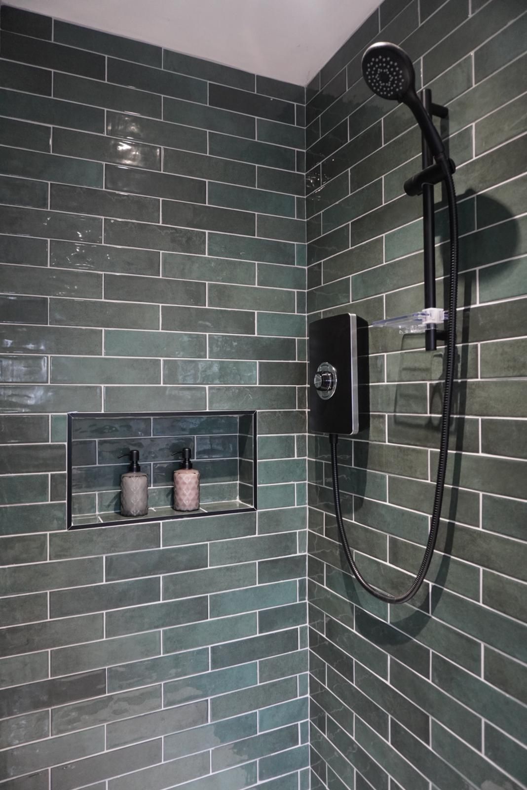 A shower with green tiles and a black shower head.