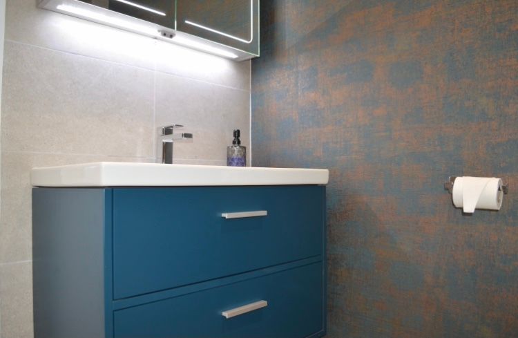 A bathroom with a blue vanity , sink , mirror and toilet paper.