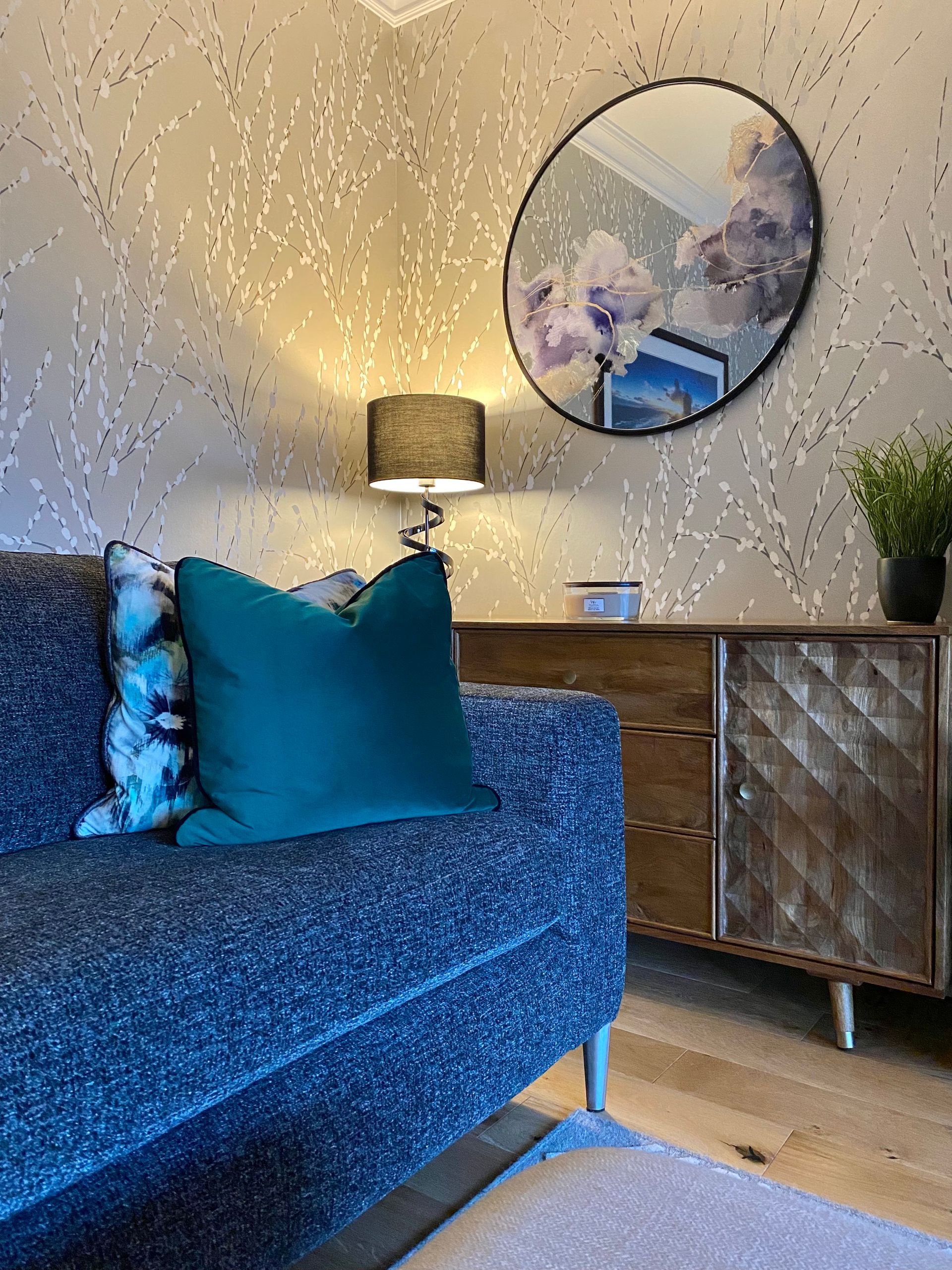 A living room with a couch , dresser , lamp and mirror.