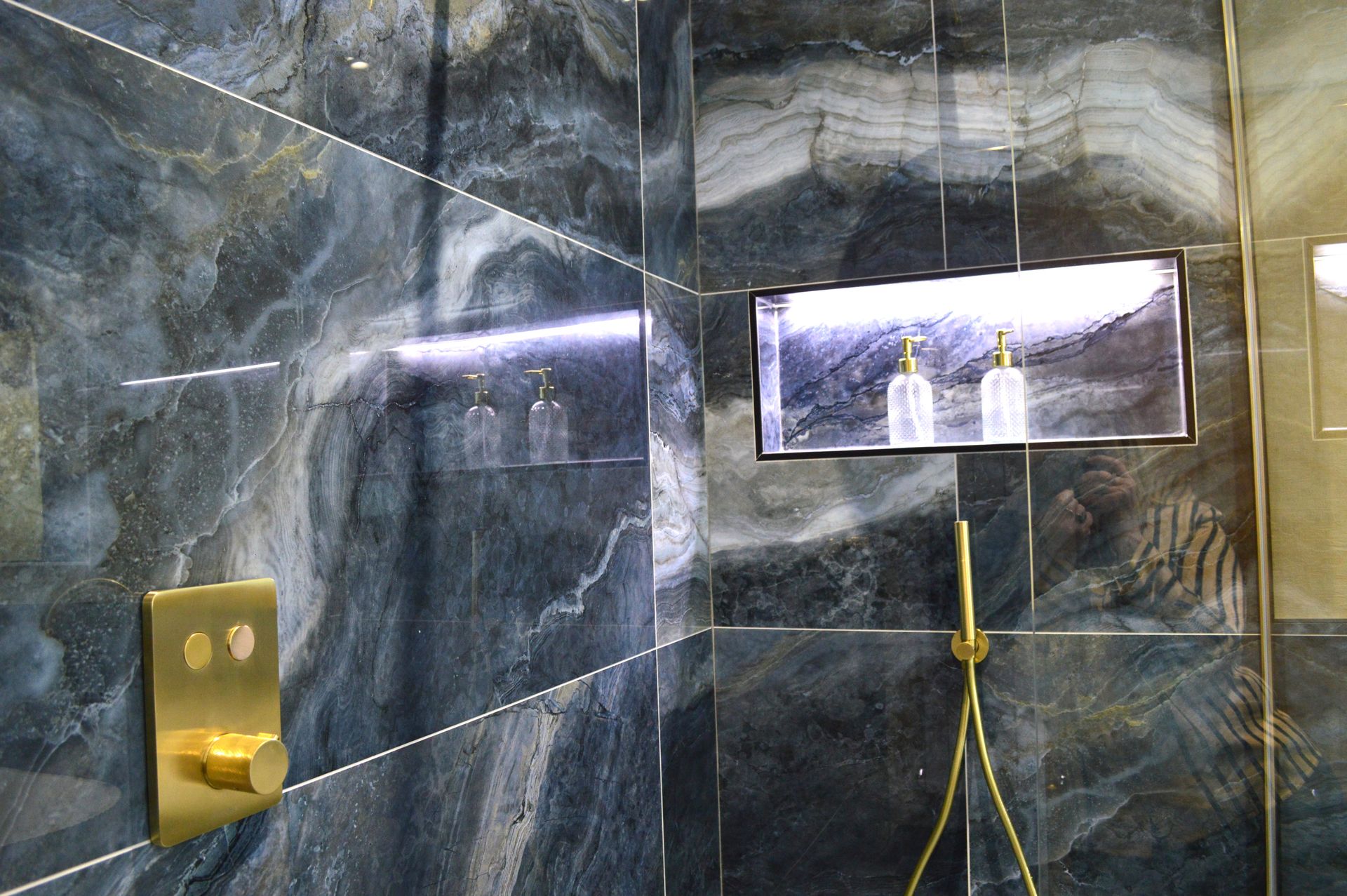 A bathroom with blue tiles and a gold shower head