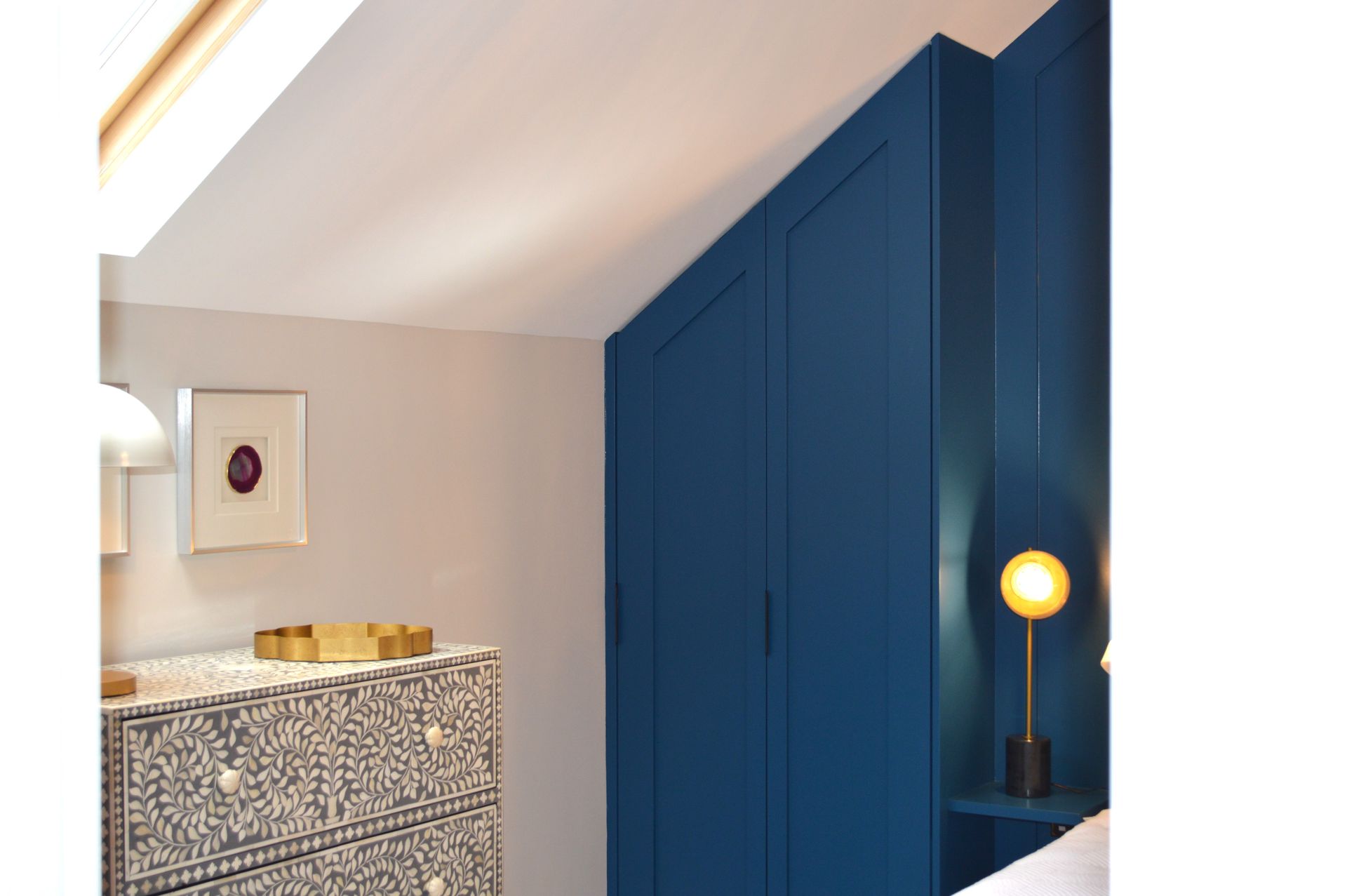 A bedroom with blue walls , a dresser and a lamp.