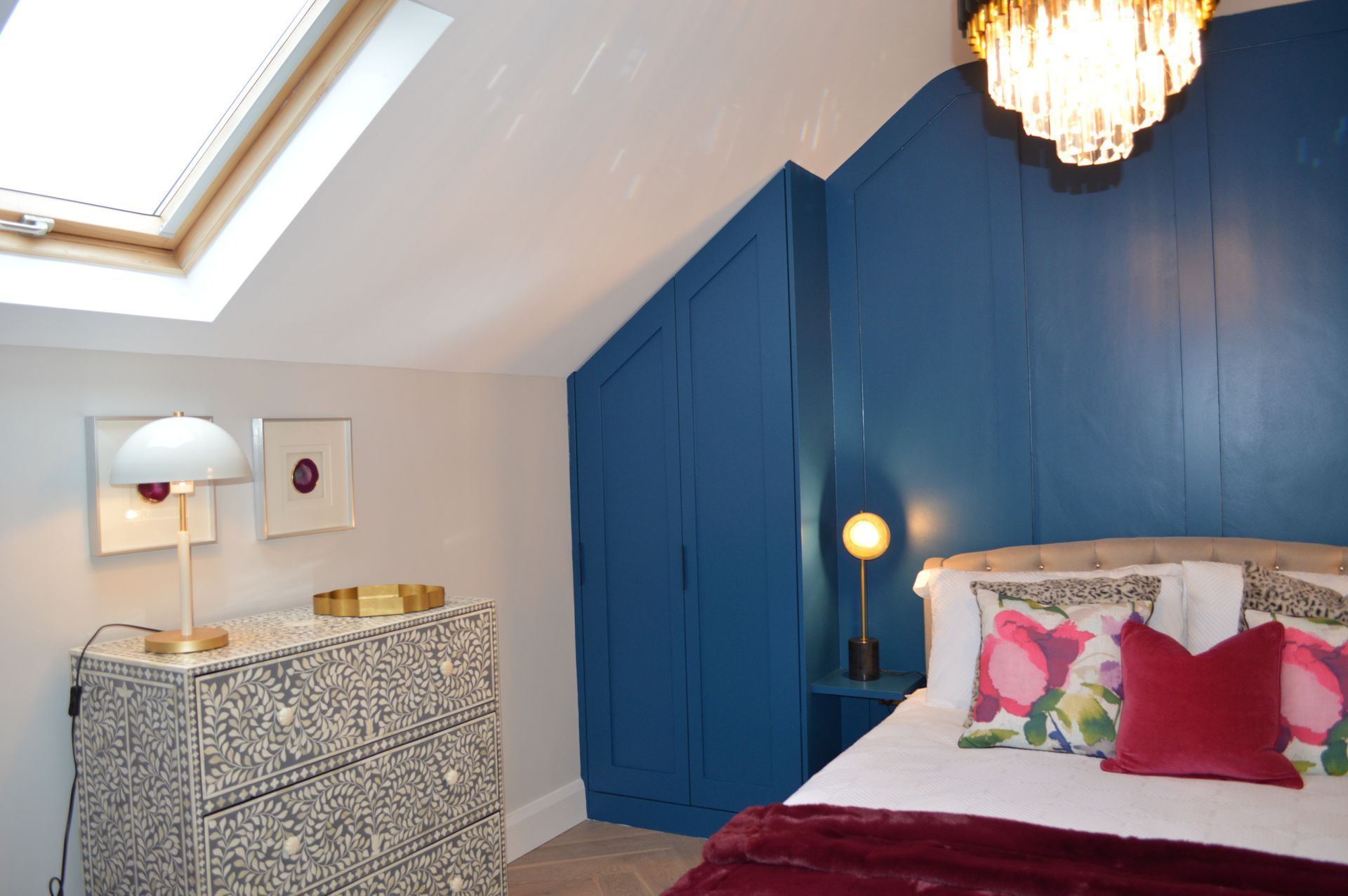 A bedroom with a bed , dresser , lamp and skylight.