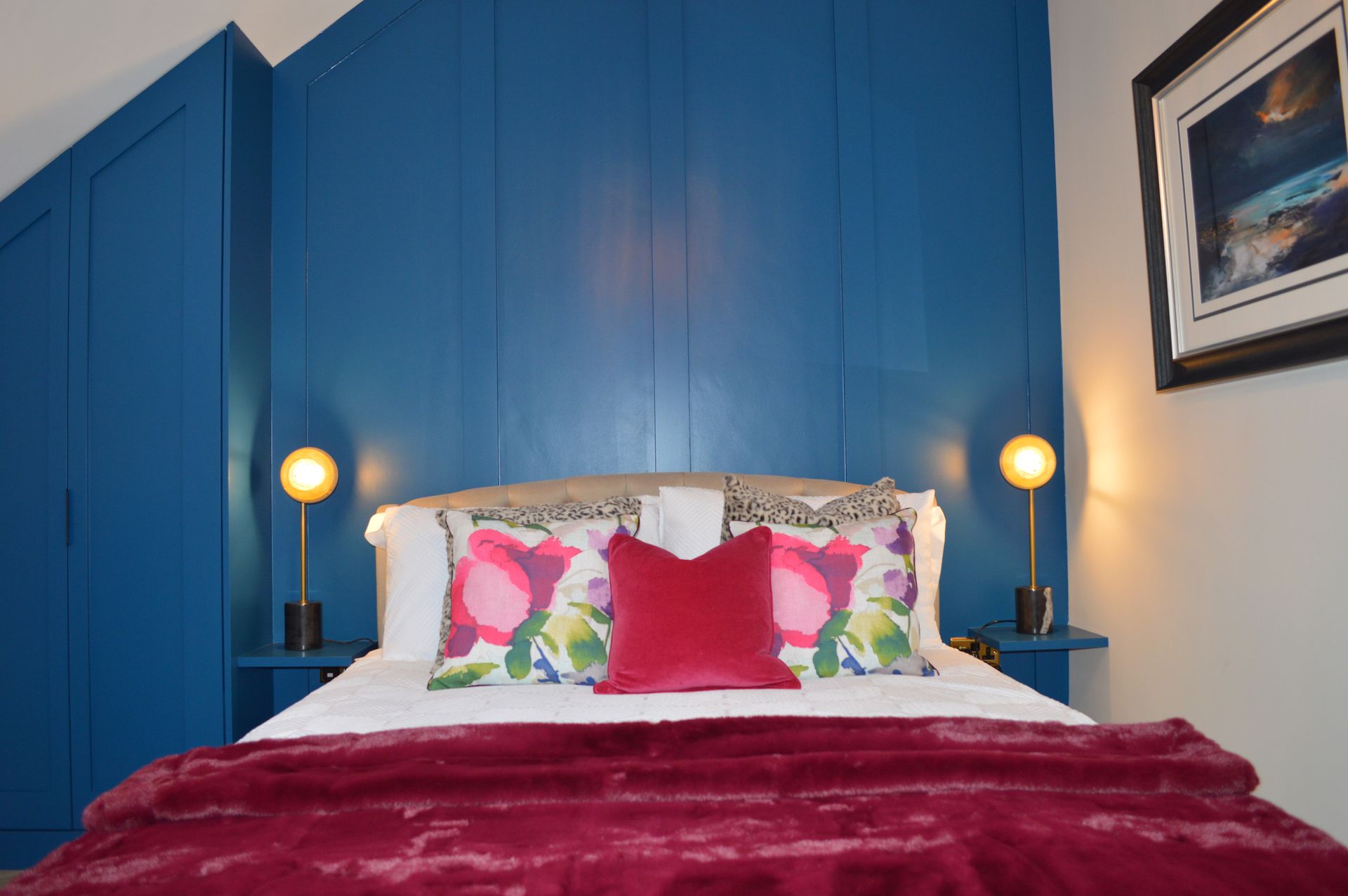 A bed with a purple blanket and pillows in a bedroom with blue walls.