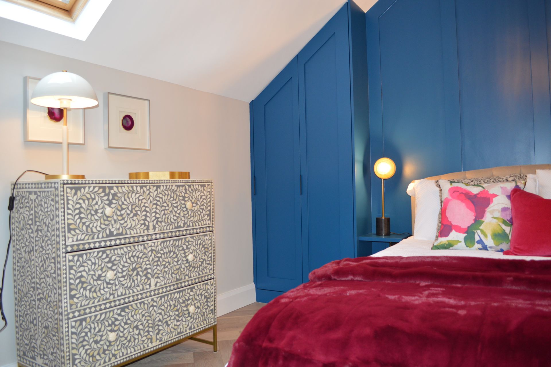 A bedroom with a bed , dresser , lamp and blue walls.