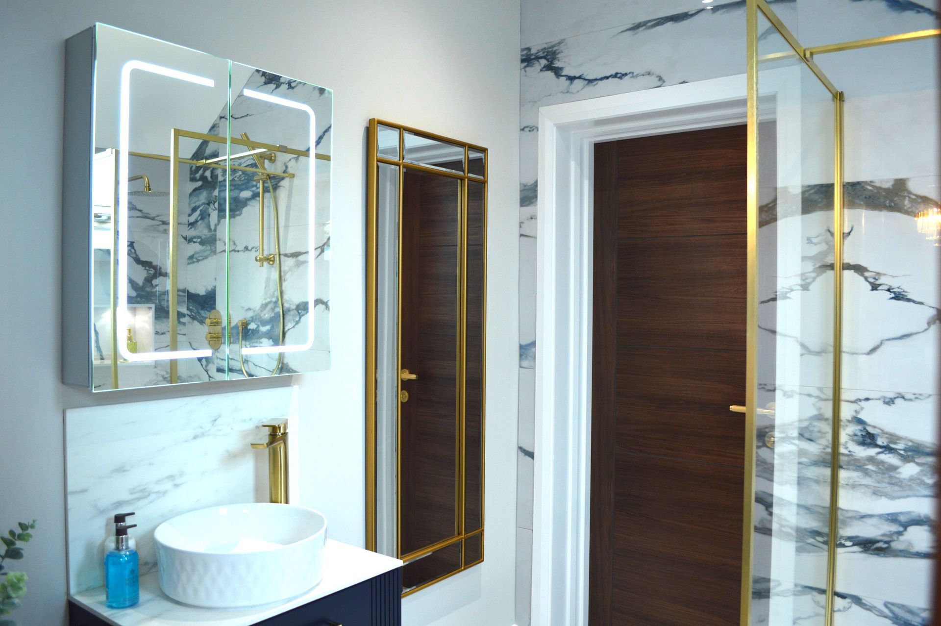 A bathroom with a sink , mirrors , and a walk in shower.