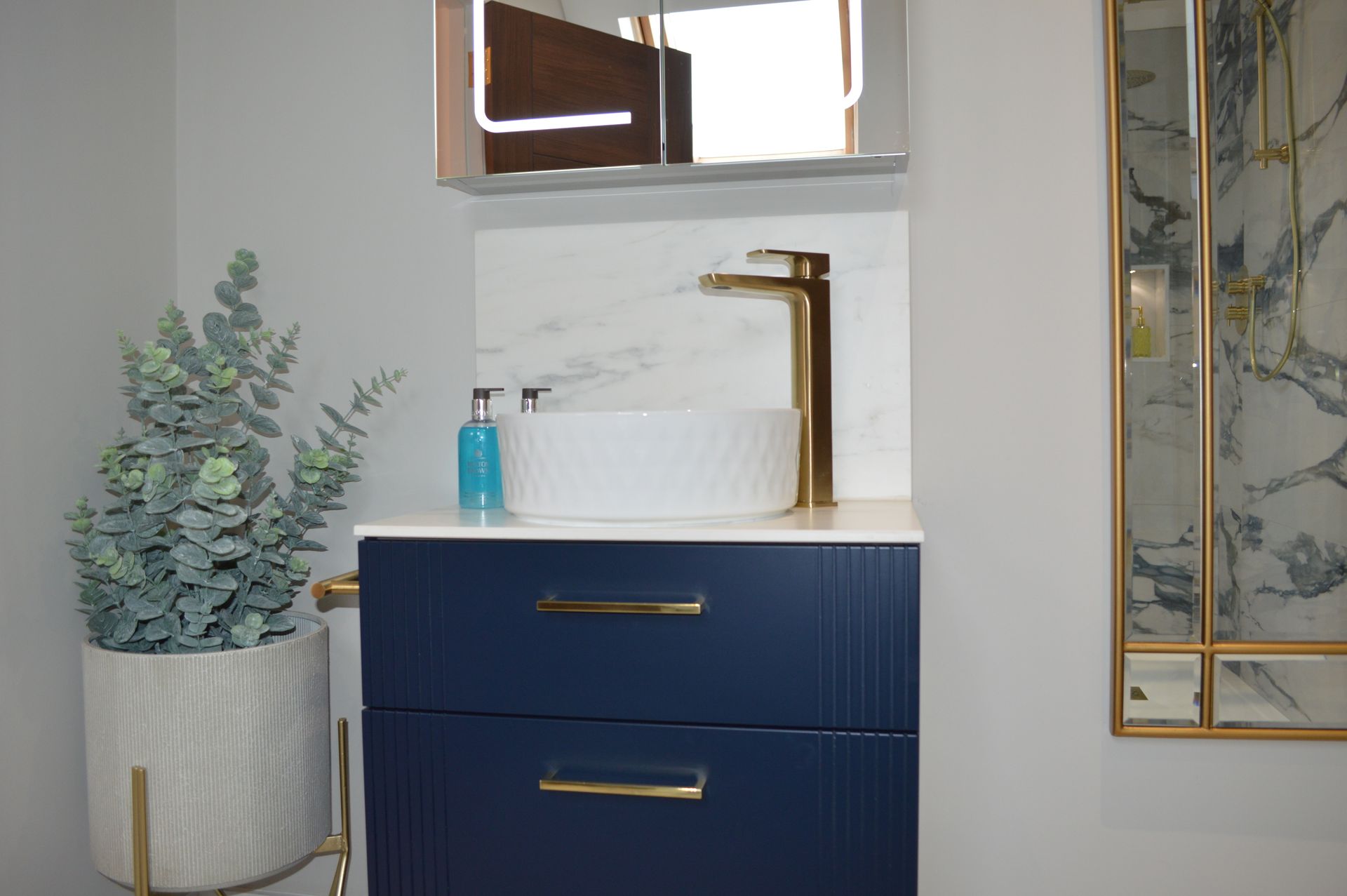 A bathroom with a blue vanity , sink , mirror and plant.