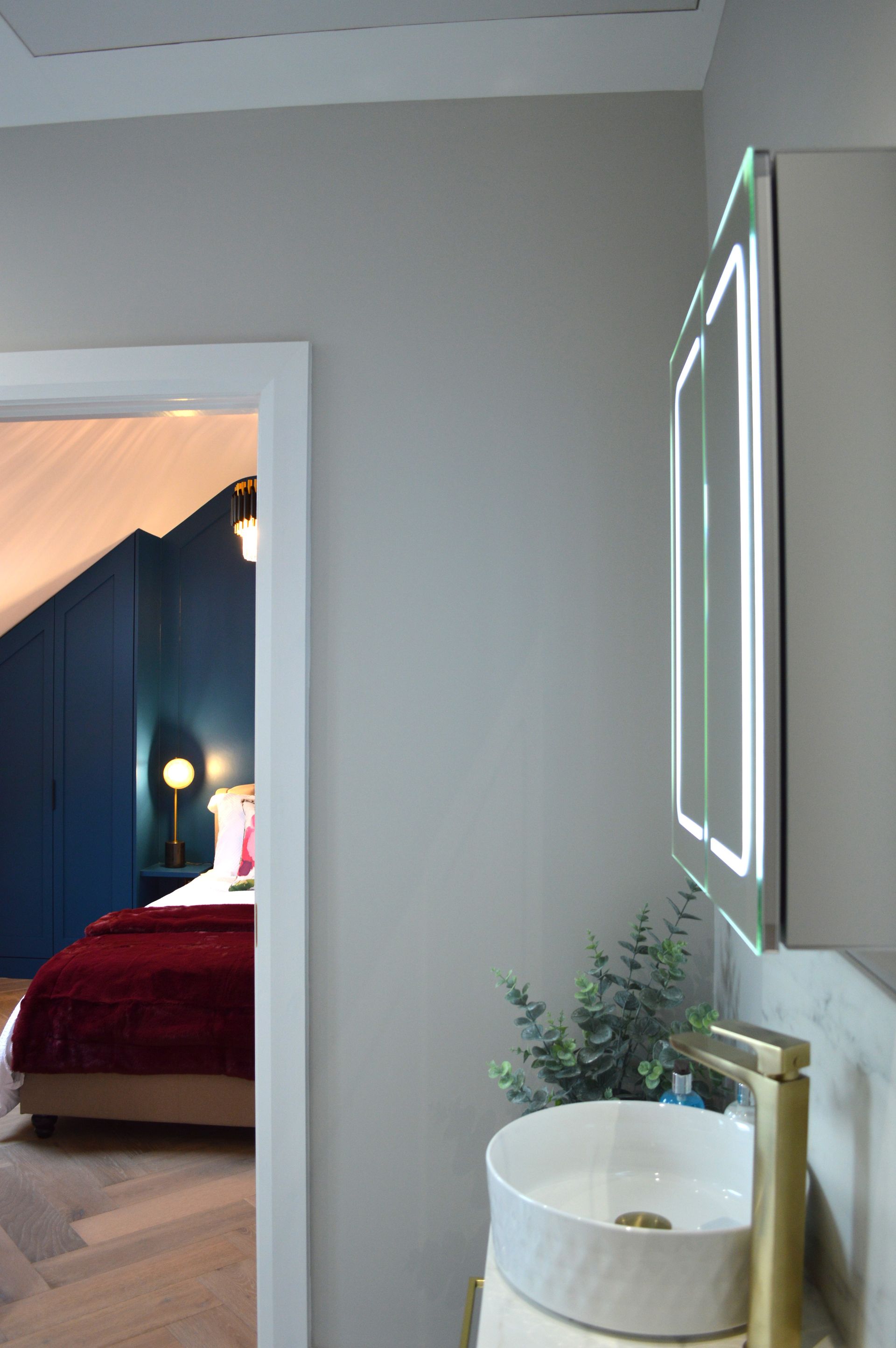 A bathroom with a sink , mirror and a bed in the background.