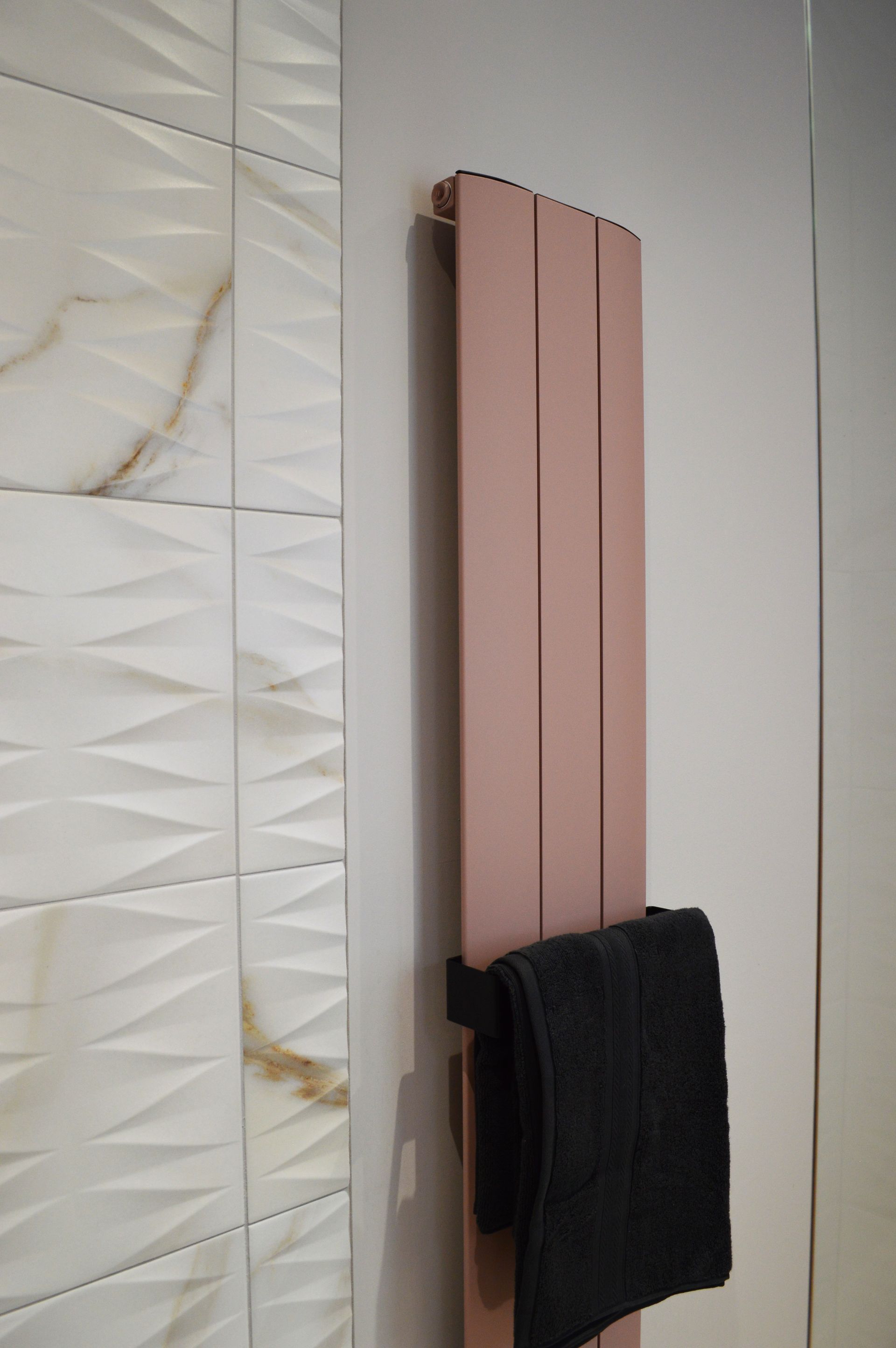 A black towel is hanging on a pink radiator in a bathroom.