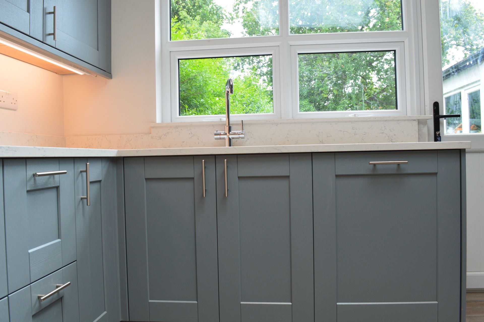 A kitchen with gray cabinets , a sink , and a window.