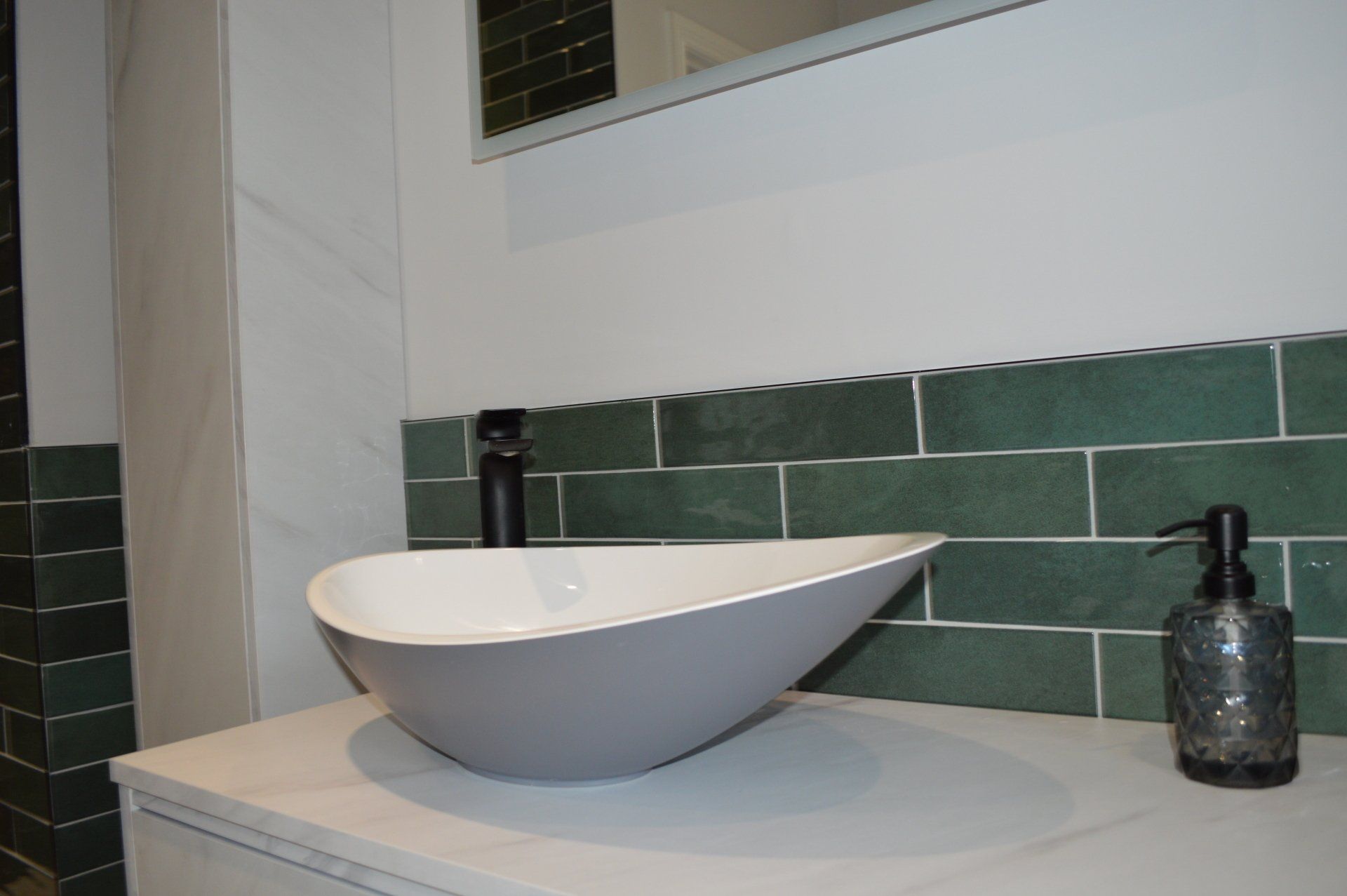 A bathroom sink with green tiles and a soap dispenser