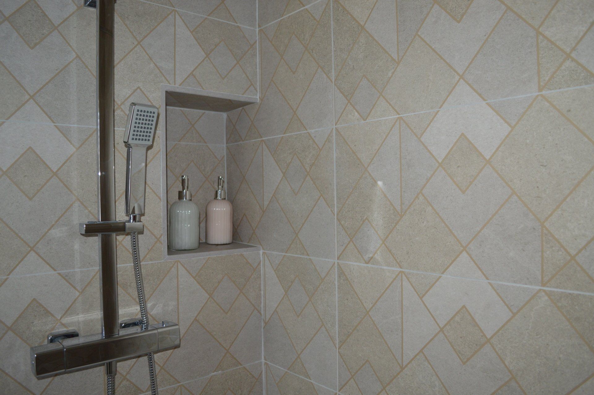 A bathroom with a shower head and a shelf with bottles on it.