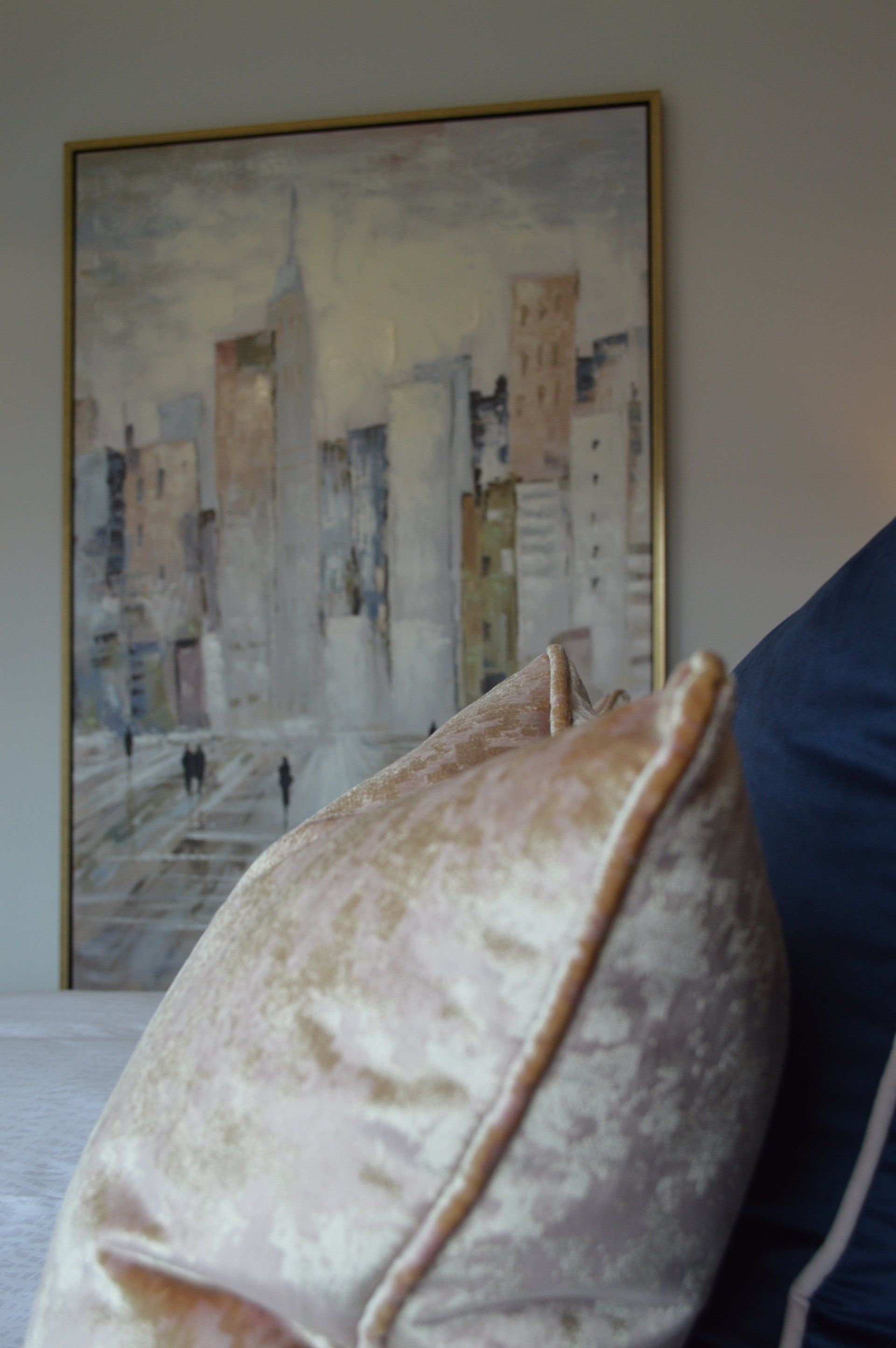 A pillow is sitting on a bed in front of a painting of a city