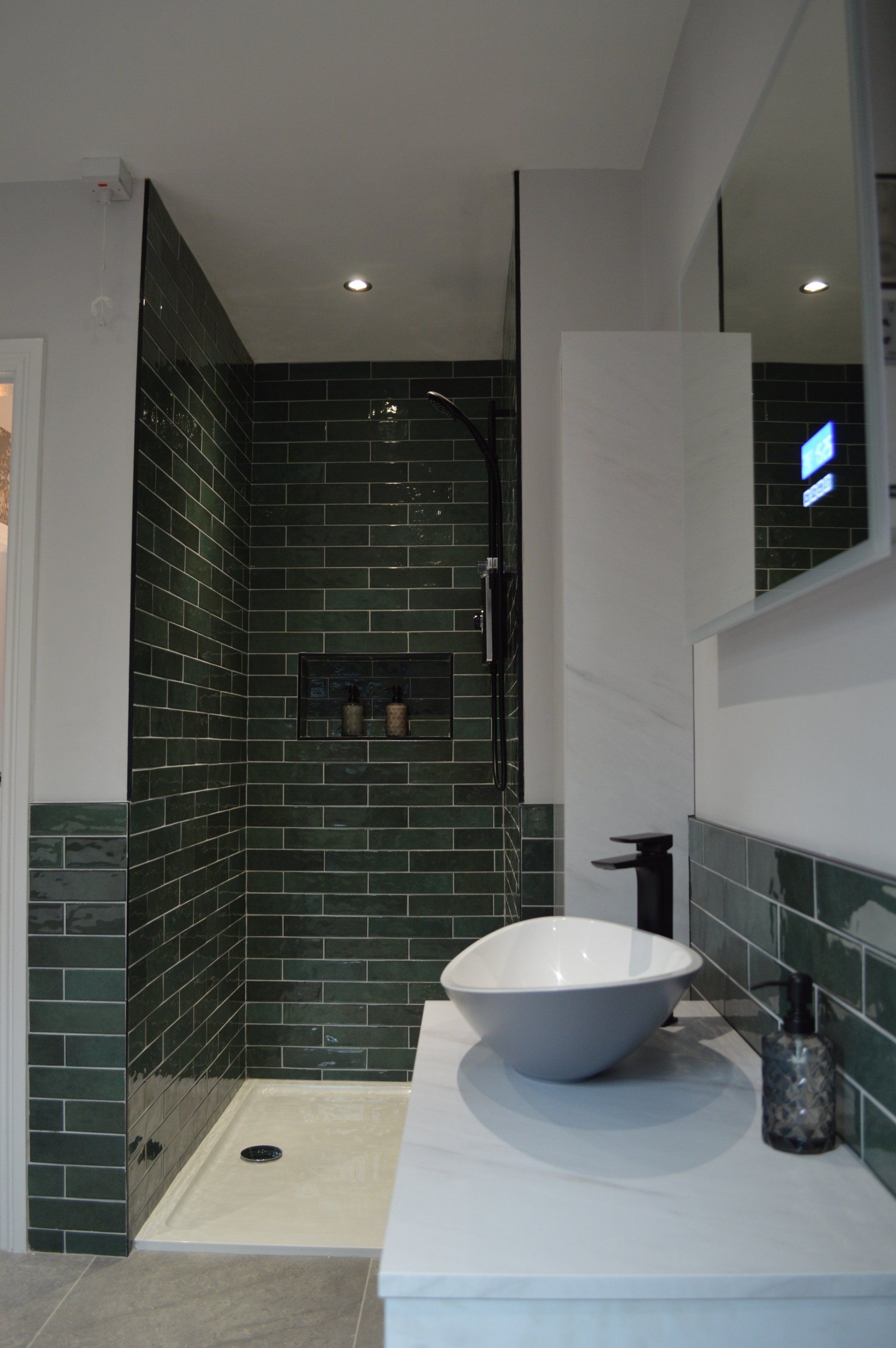 A bathroom with green tiles , a sink , and a walk in shower.
