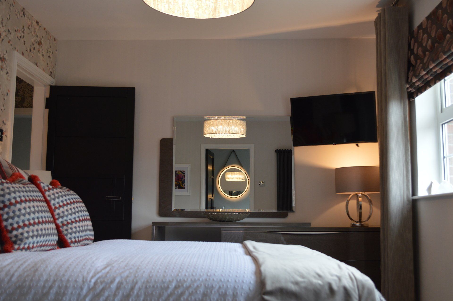 A bedroom with a bed , television , mirror and lamp.