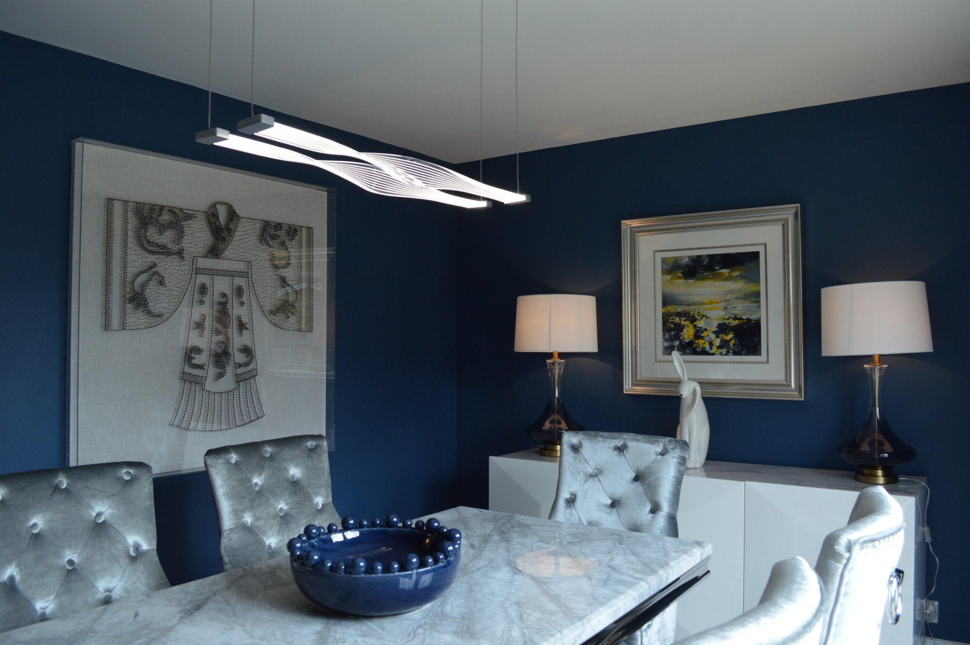 A dining room with a table , chairs , lamps and a picture on the wall.