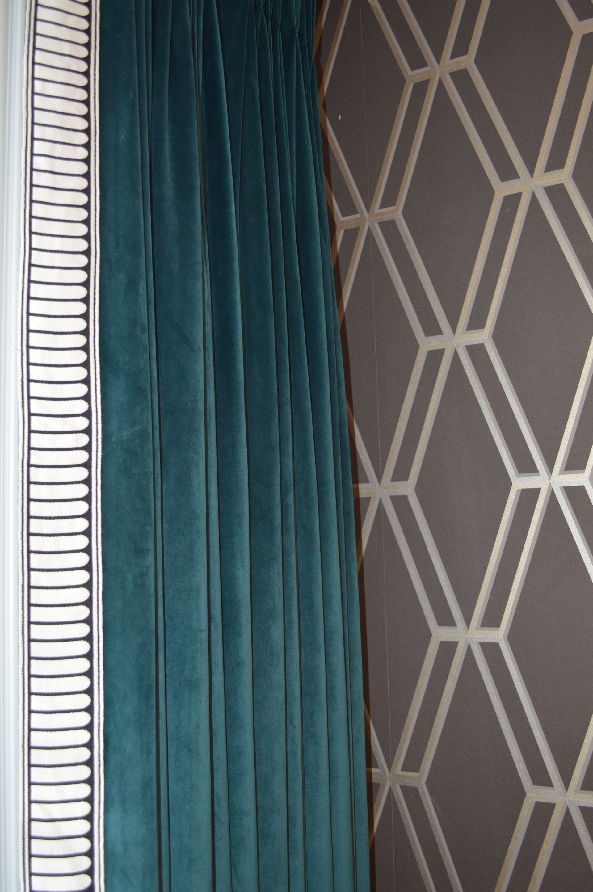 A blue curtain is hanging on a window next to a wall with a geometric pattern.