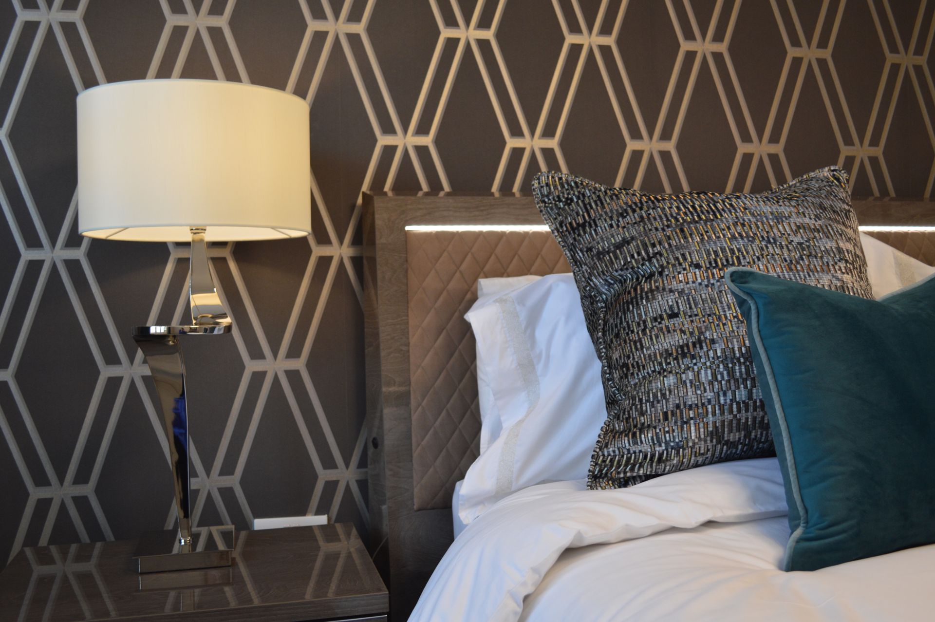 A bedroom with a bed , nightstand , lamp and pillows.