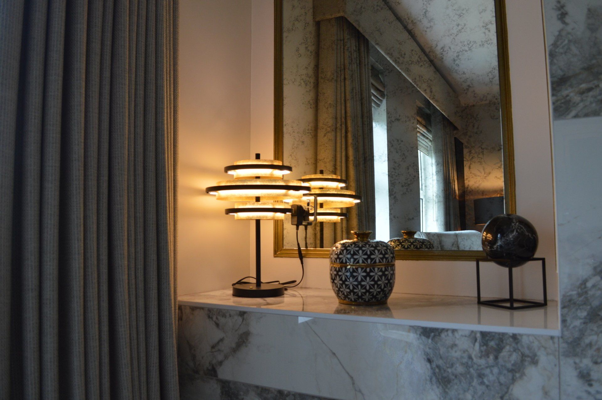 A lamp is sitting on a table next to a mirror in a room.