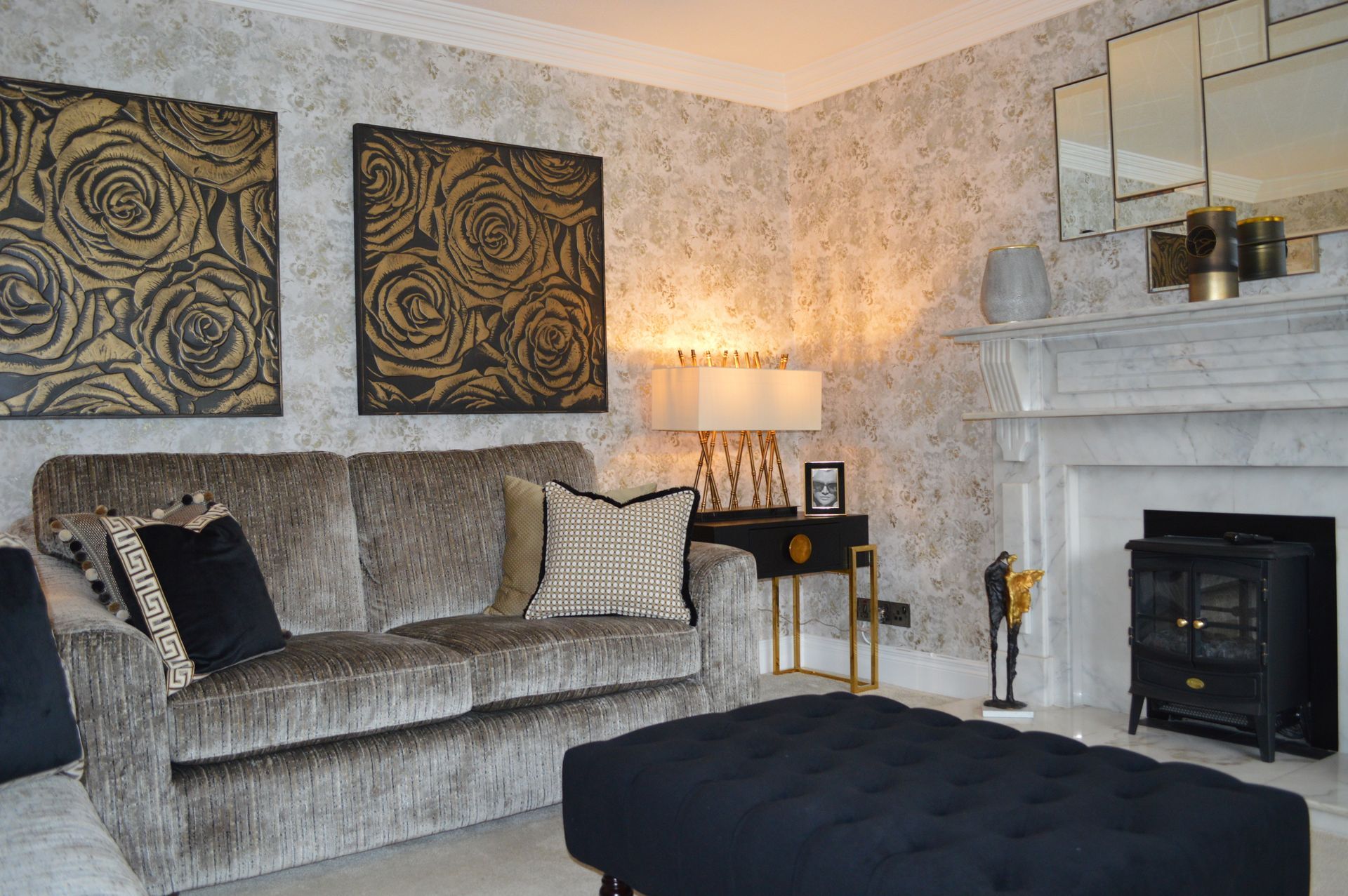 A living room with a couch , ottoman , fireplace and paintings on the wall.