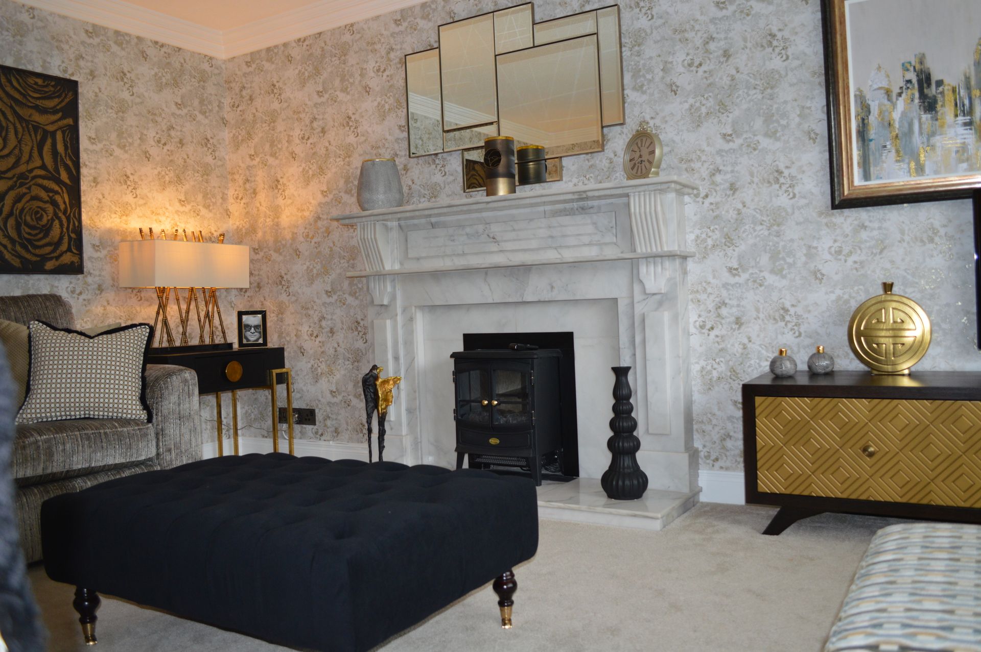 A living room with a fireplace and a black ottoman