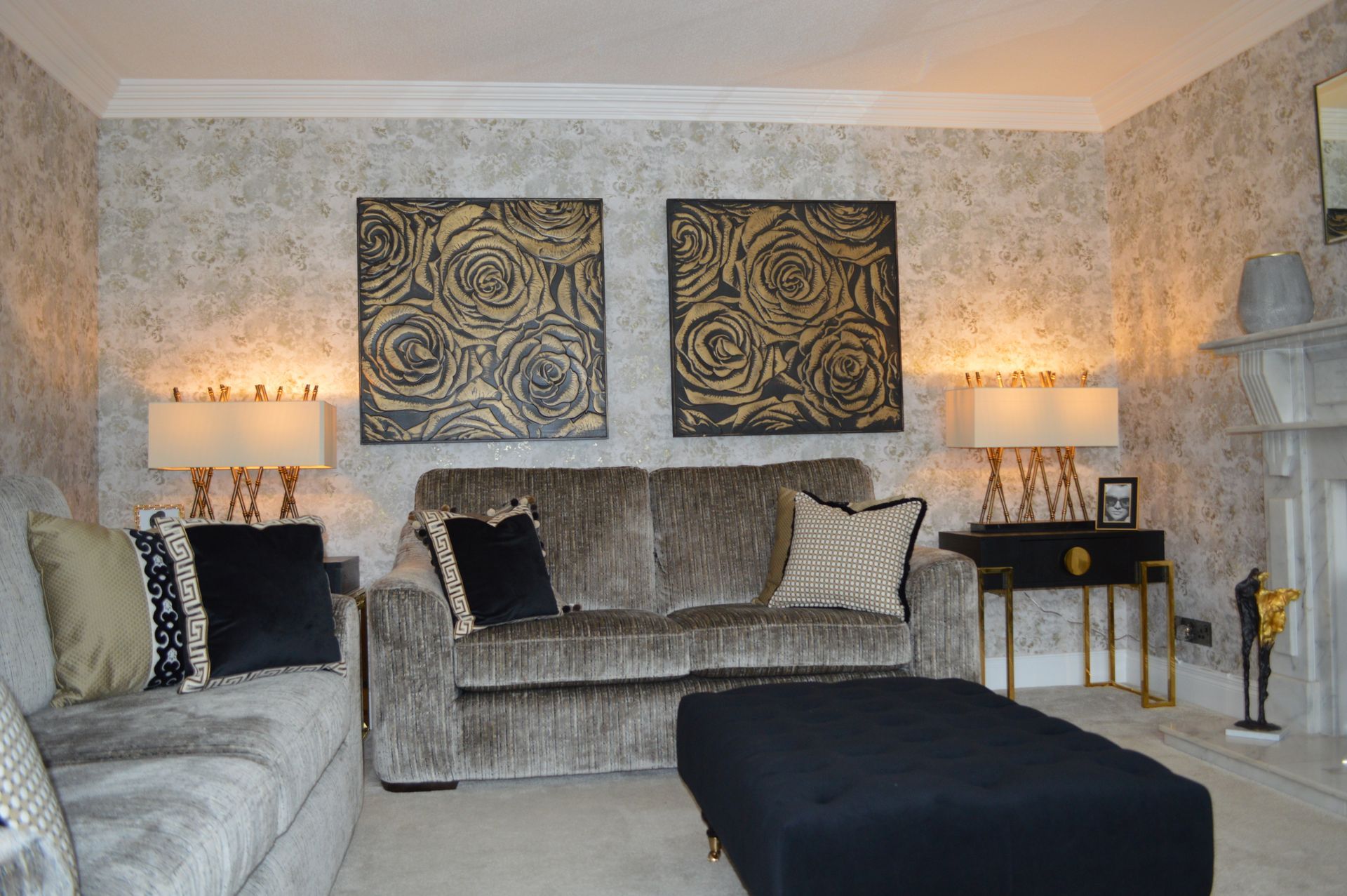 A living room with a couch , ottoman , lamps and two paintings on the wall.