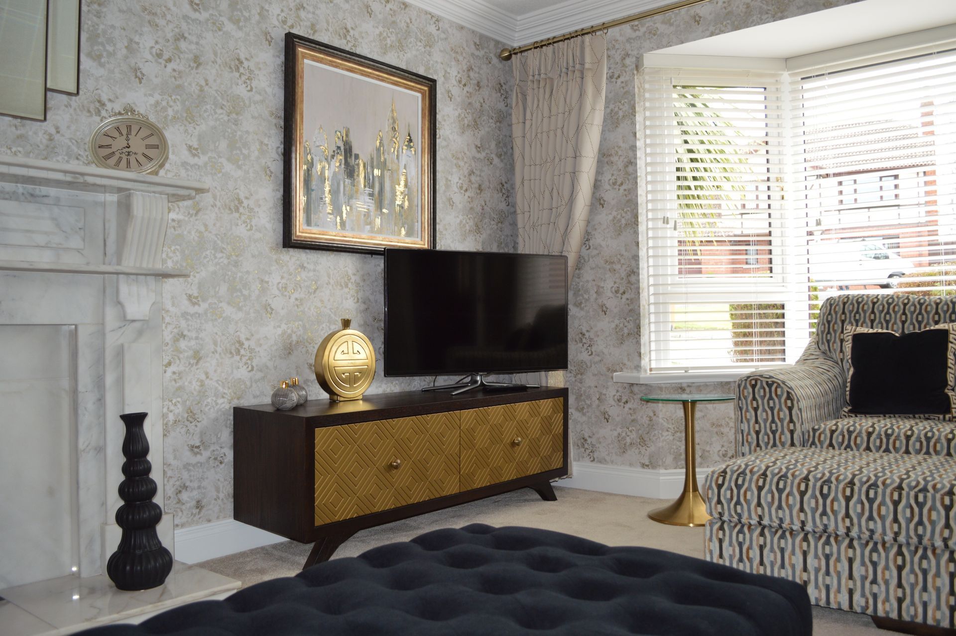 A living room with a flat screen tv , ottoman , chair and fireplace.